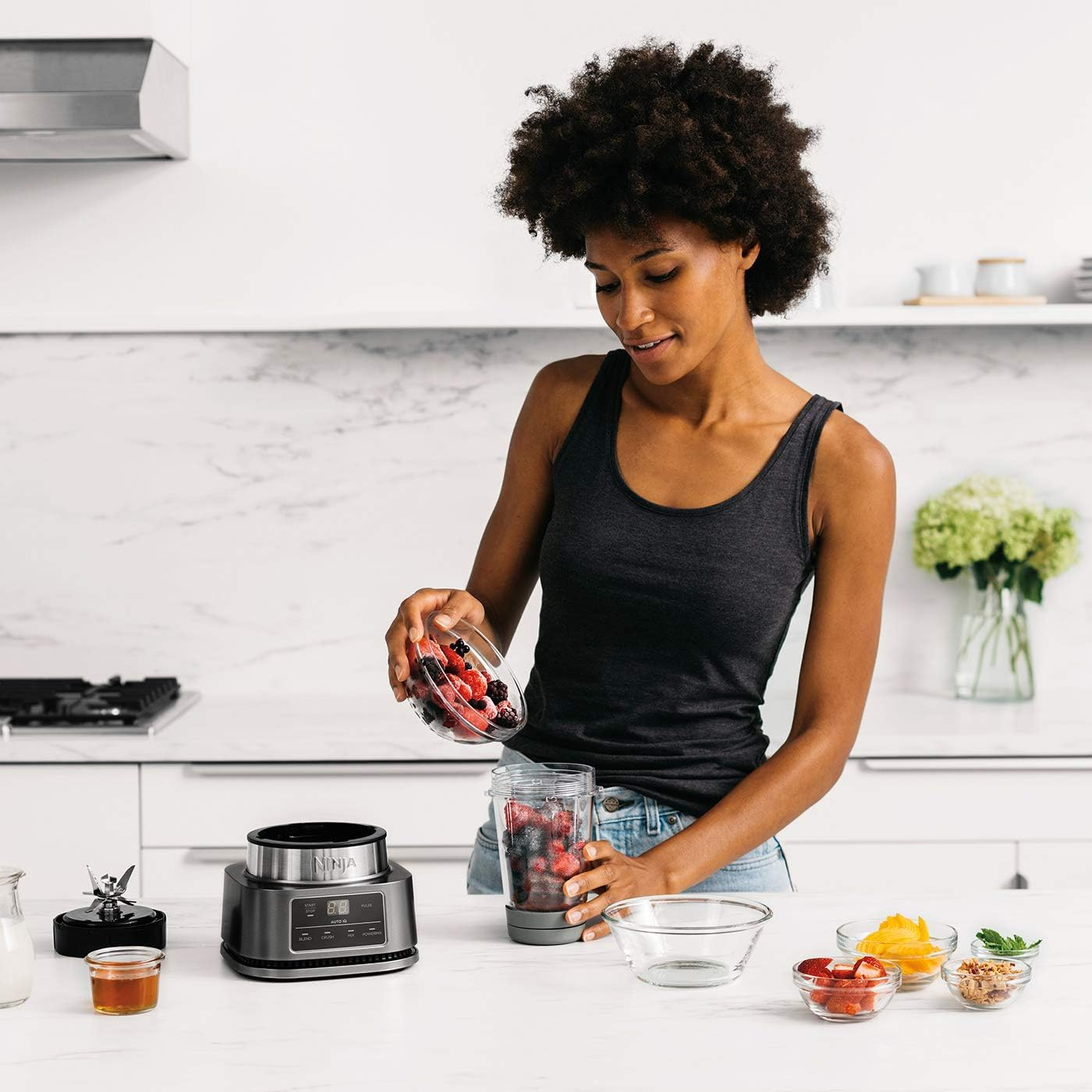 Eine Frau gießt Beeren in einen Ninja-Mixer, weitere Zutaten befinden sich in der Nähe.