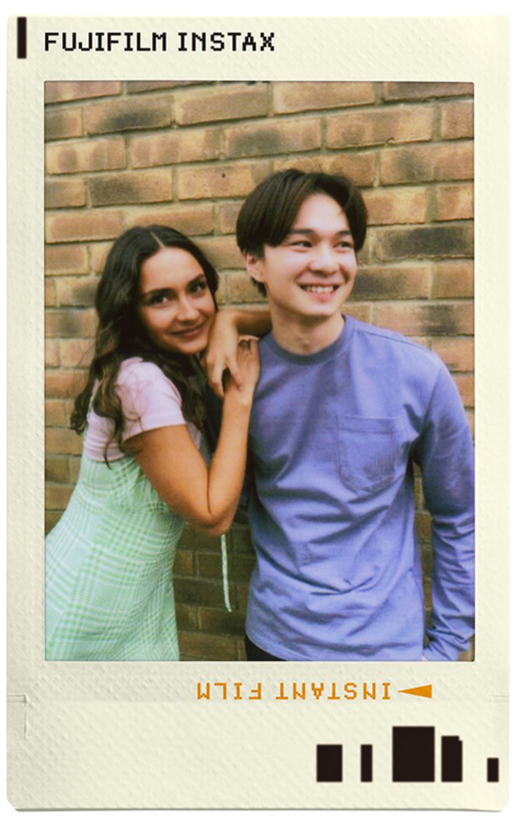 Két ember áll egymás mellett mosolyogva, polaroid keretben.