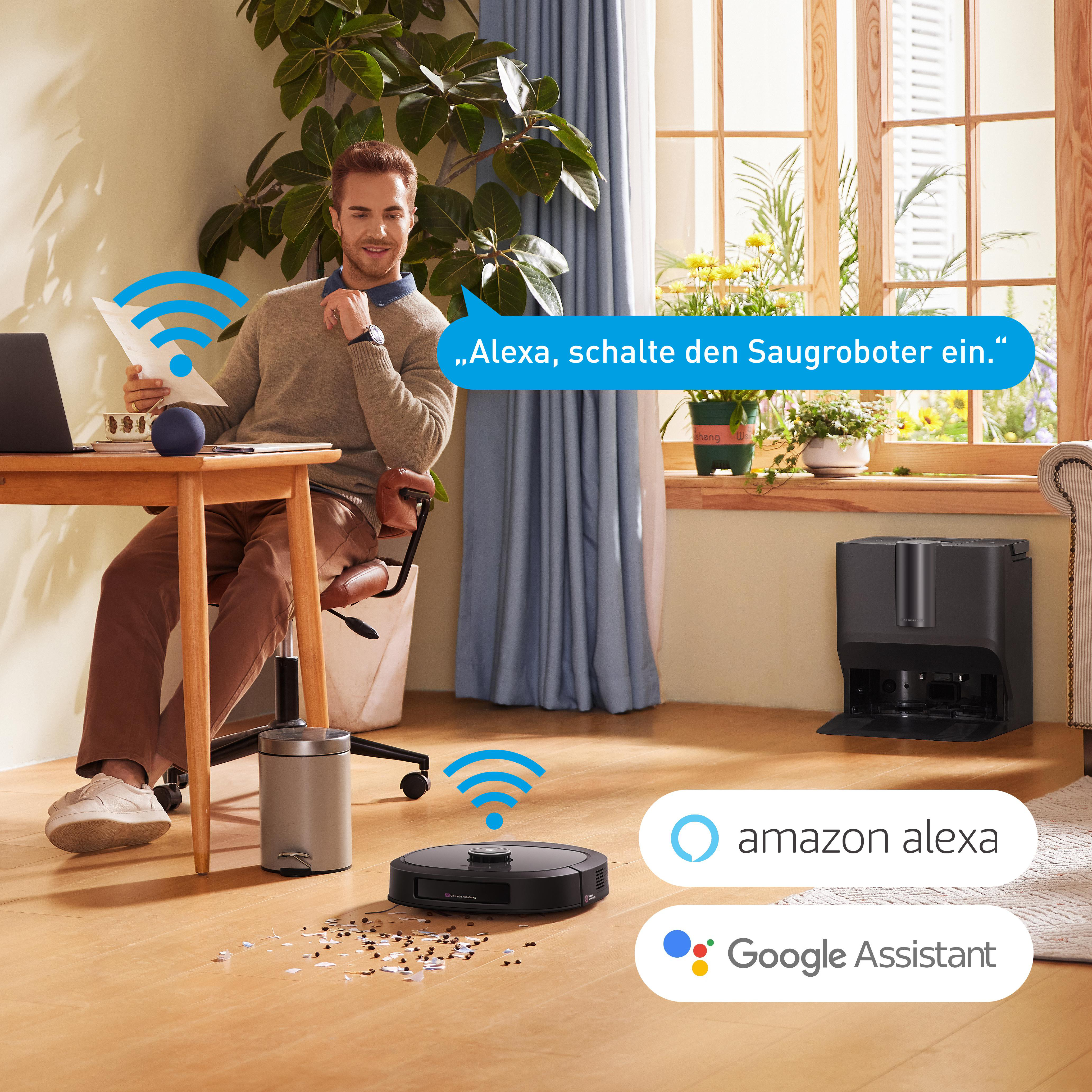 Ein Mann sitzt am Schreibtisch, während ein Roboter-Staubsauger den Boden reinigt. Alexa- und Google Assistant-Logos.