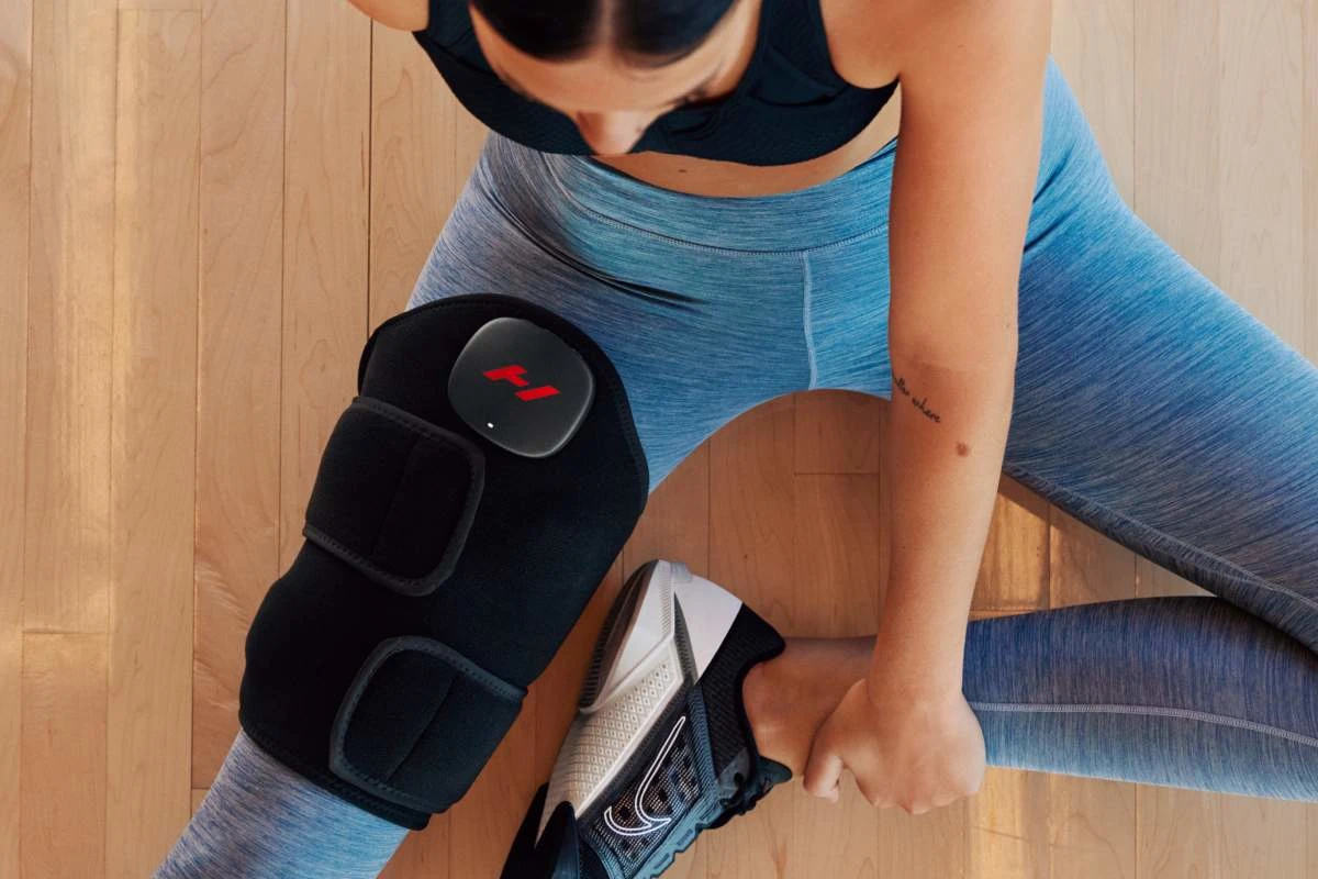 Nő térdrögzítővel és sportruhában, fa padlón ül.