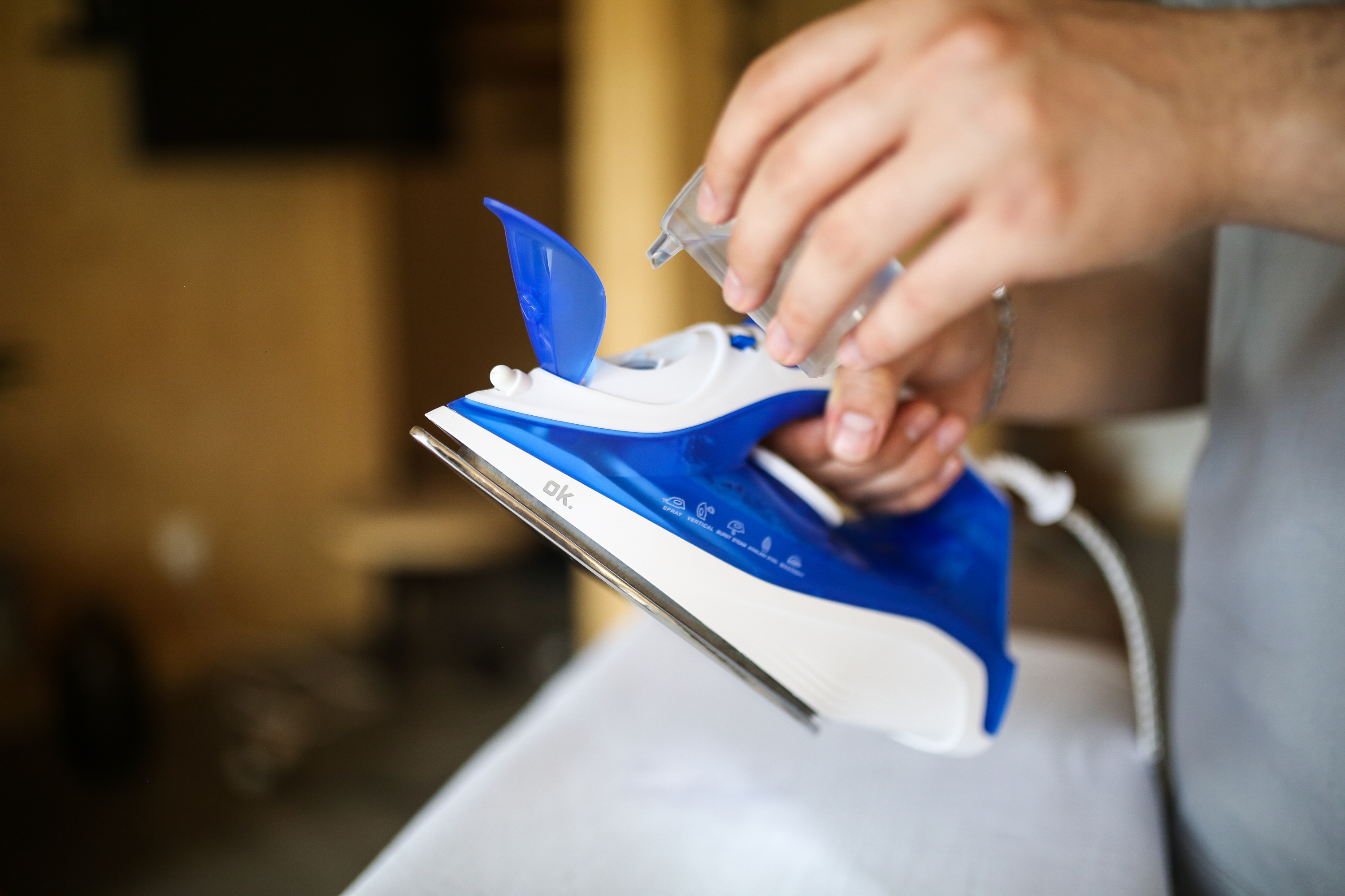 Niebiesko-białe żelazko napełniane wodą przez dłoń osoby trzymającej mały pojemnik.