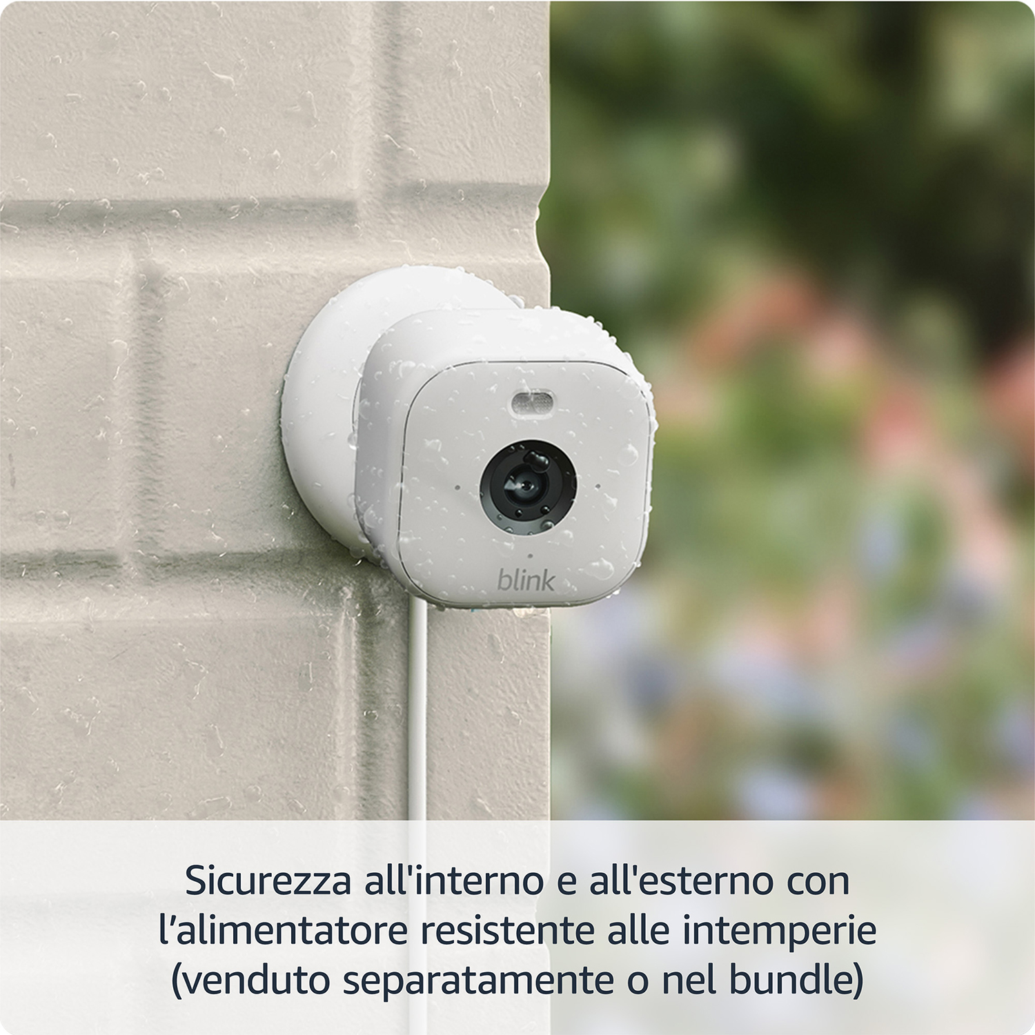 Telecamera di sicurezza bianca attaccata a un muro di mattoni, goccioline d'acqua visibili. Sfondo sfocato.