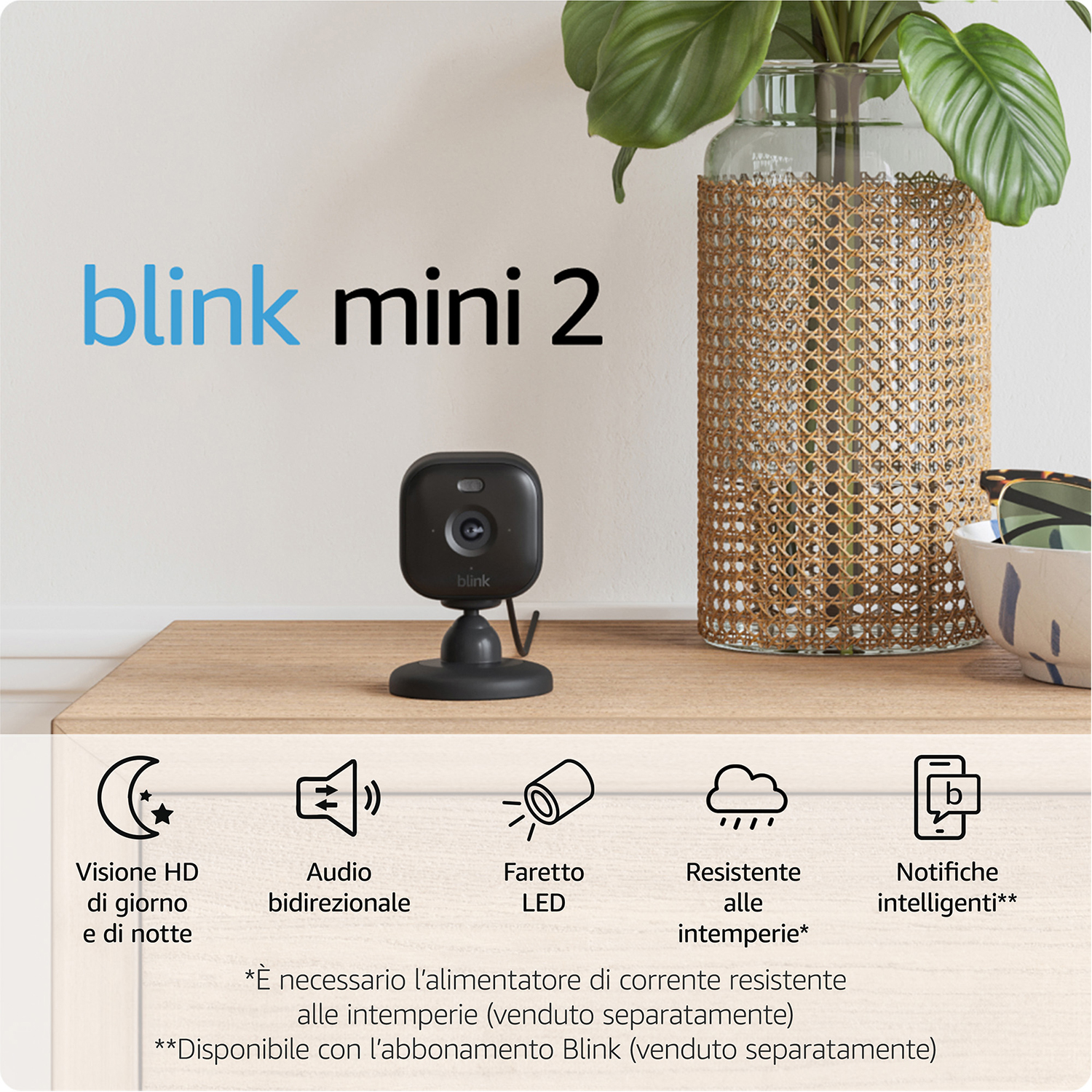 Una telecamera di sicurezza Blink Mini 2 nera su un tavolo di legno vicino a un vaso e testo con funzioni.