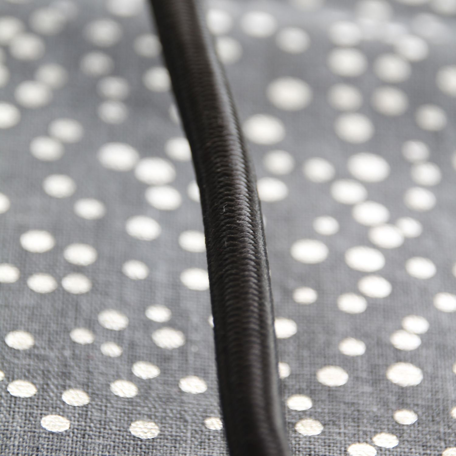 Close-up of a black, textured cable against a gray fabric with white polka dots.