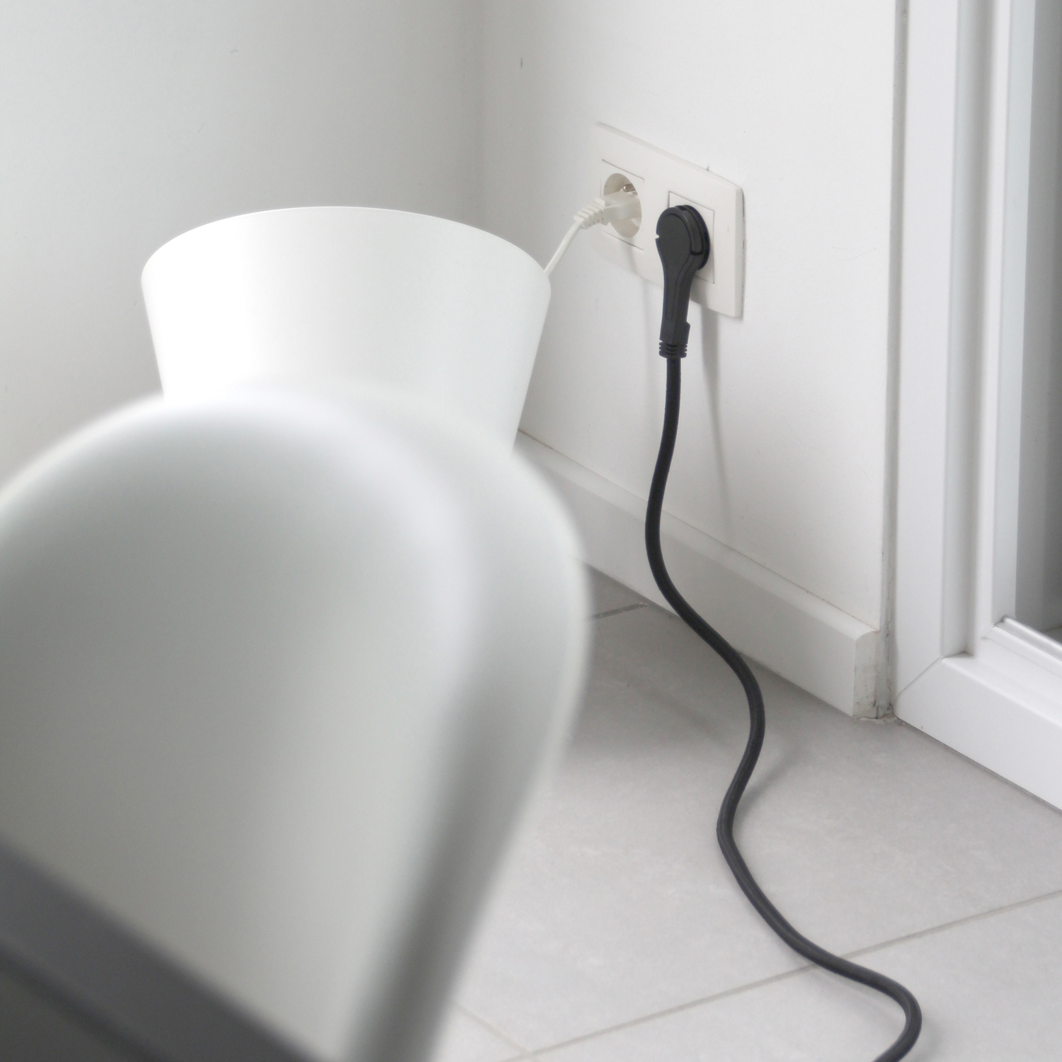 White vase with a black power cord plugged into a wall outlet.