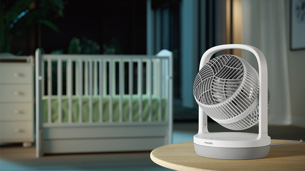 Fehér és szürke Philips ventilátor az asztalon, háttérben kiságy.