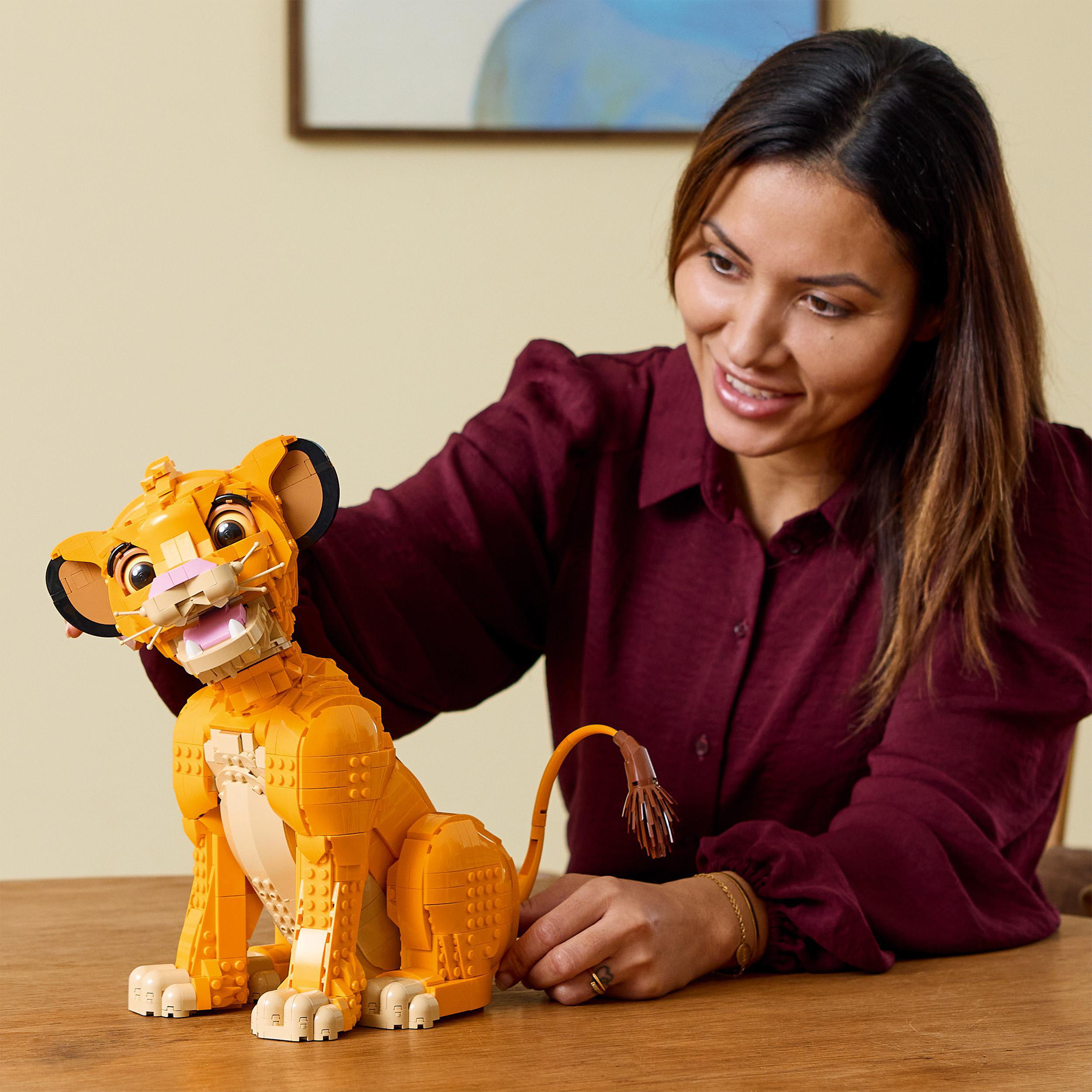 Eine Frau lächelt, während sie eine Lego Simba Figur zusammensetzt.