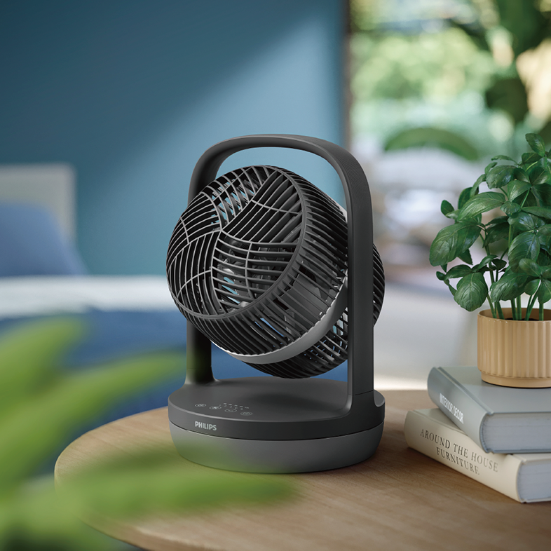Egy fekete ventilátor az asztalon, fogantyúval és hálós ráccsal.