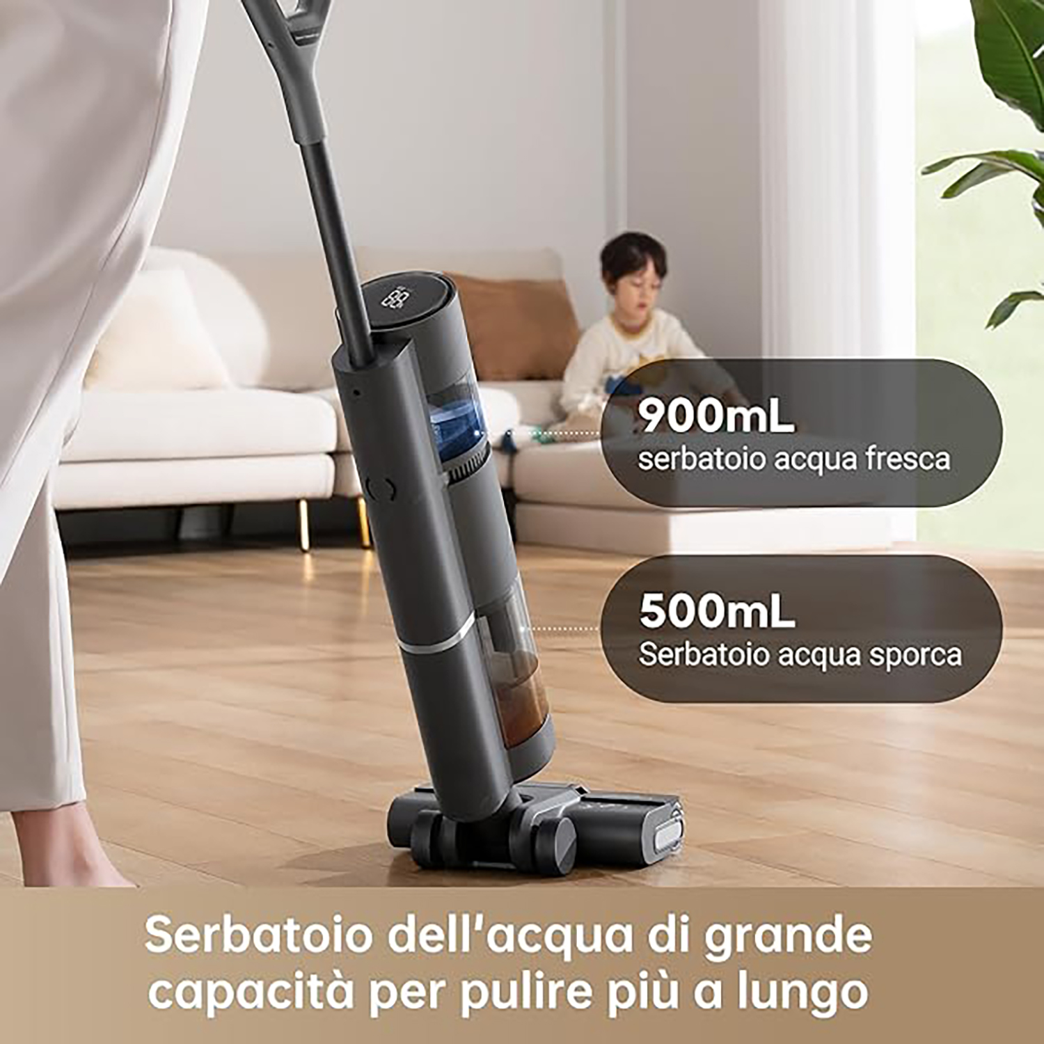 Un aspirapolvere senza fili grigio scuro con serbatoi d'acqua e un bambino sullo sfondo.