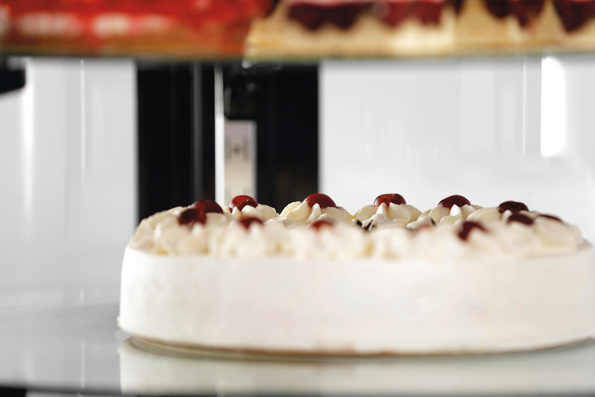 Eine weiße Torte mit Sahnetupfen und roten Früchten in einer Glasvitrine.
