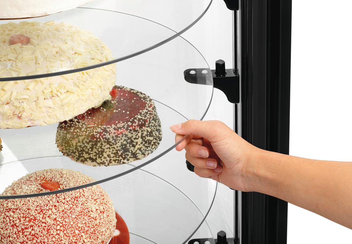 Eine Hand dreht eine Glasplatte in einer Kuchentheke mit verschiedenen Kuchen.