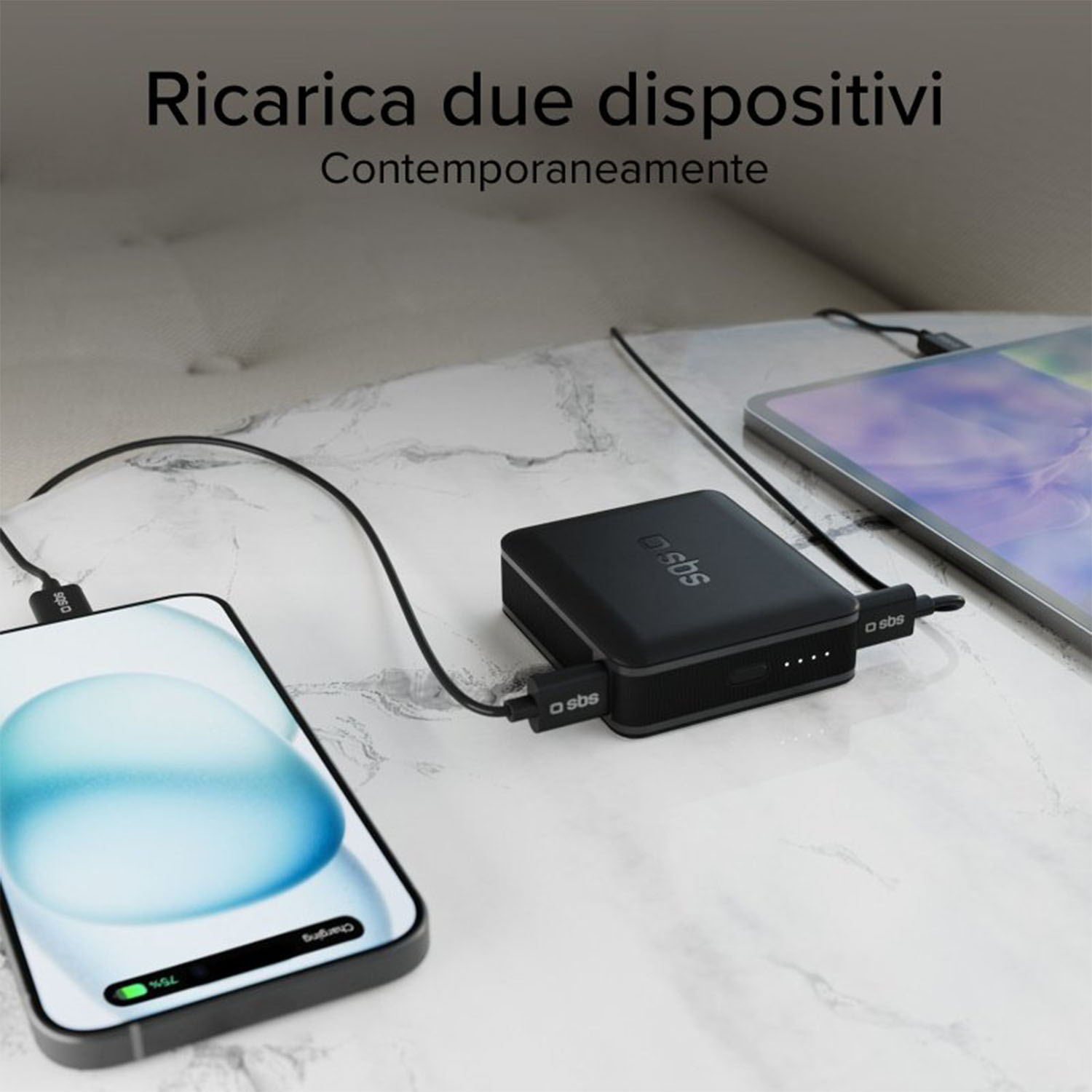 Telefono e tablet in carica con un power bank nero su una superficie di marmo.