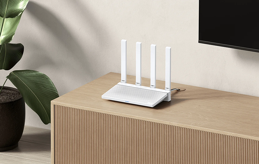 Fehér router 4 antennával fa felületen, növény és TV közelében.