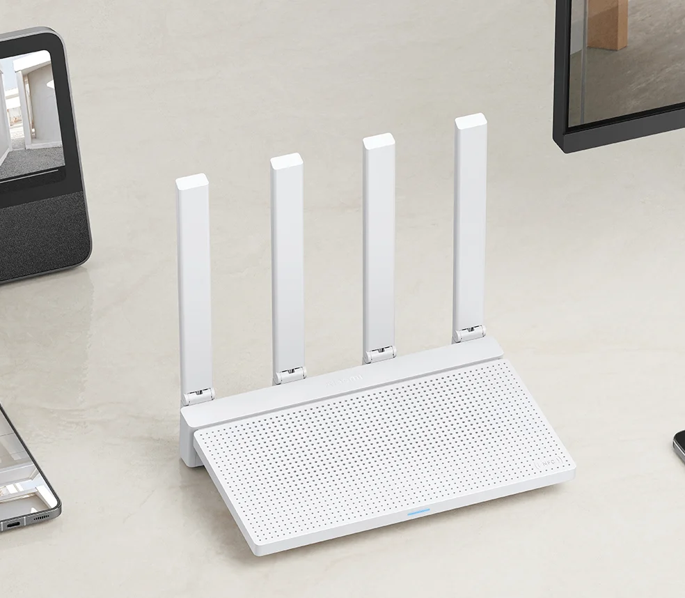 Fehér router 4 antennával fehér felületen, más eszközökkel körülvéve.