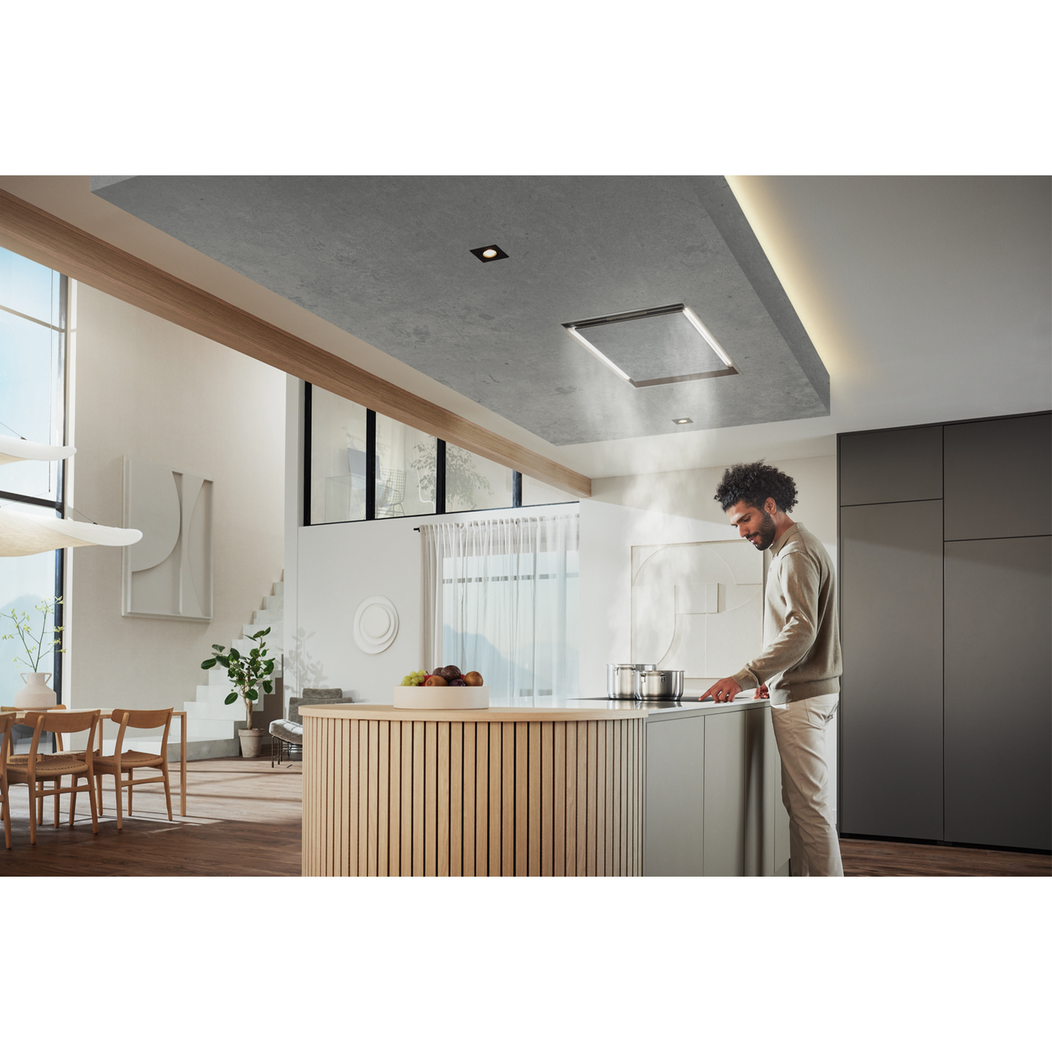 Un uomo cucina in una cucina moderna con cappa a soffitto e isola, luce naturale.