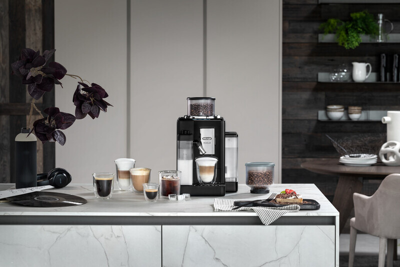 A kitchen counter with a coffee machine, coffee cups, and a tray with food on it. Background is blurred.