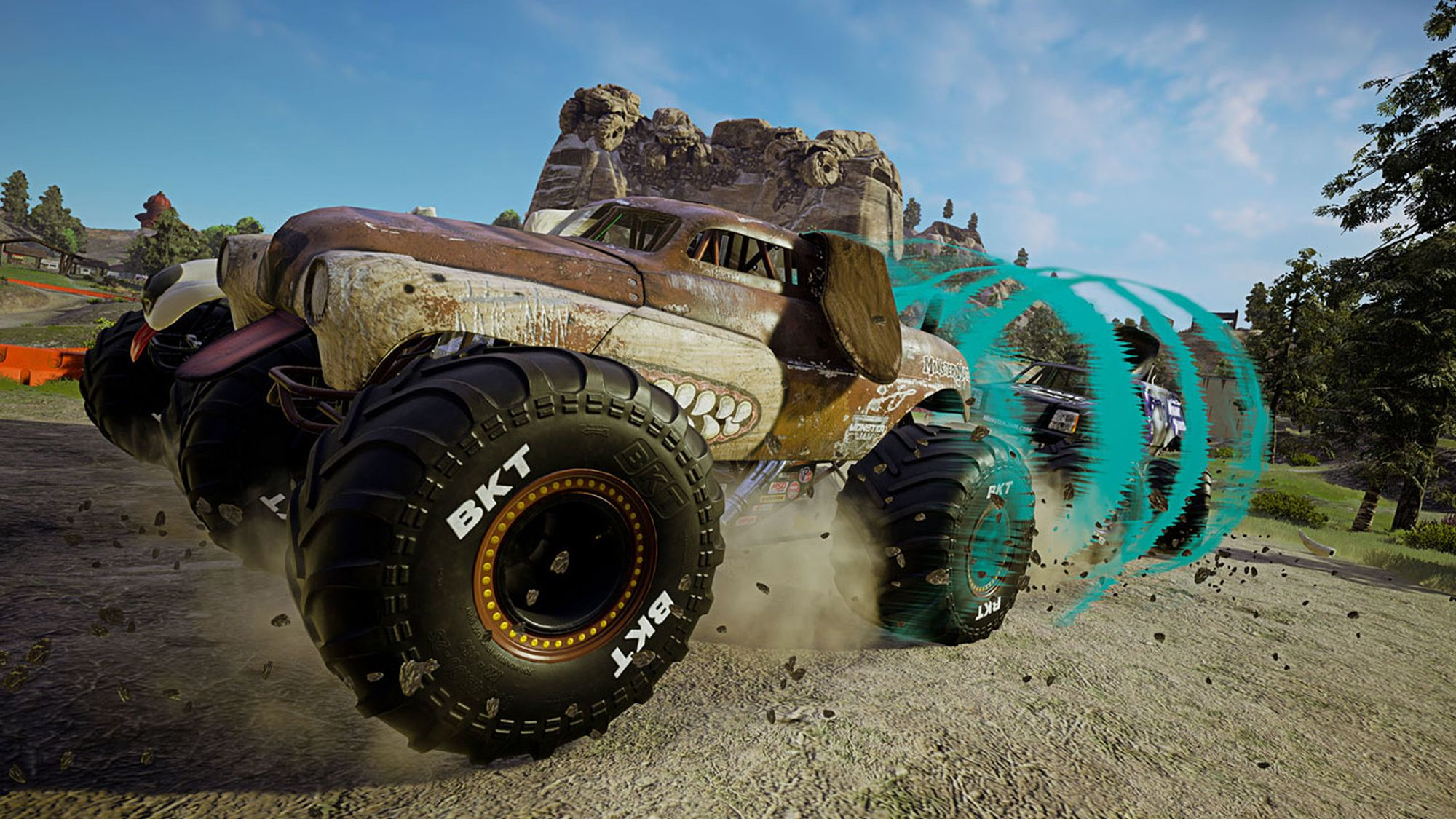 Monster truck dal design simile a un cane, che guida su una pista sterrata. Pneumatici BKT. Alberi e cielo sullo sfondo.