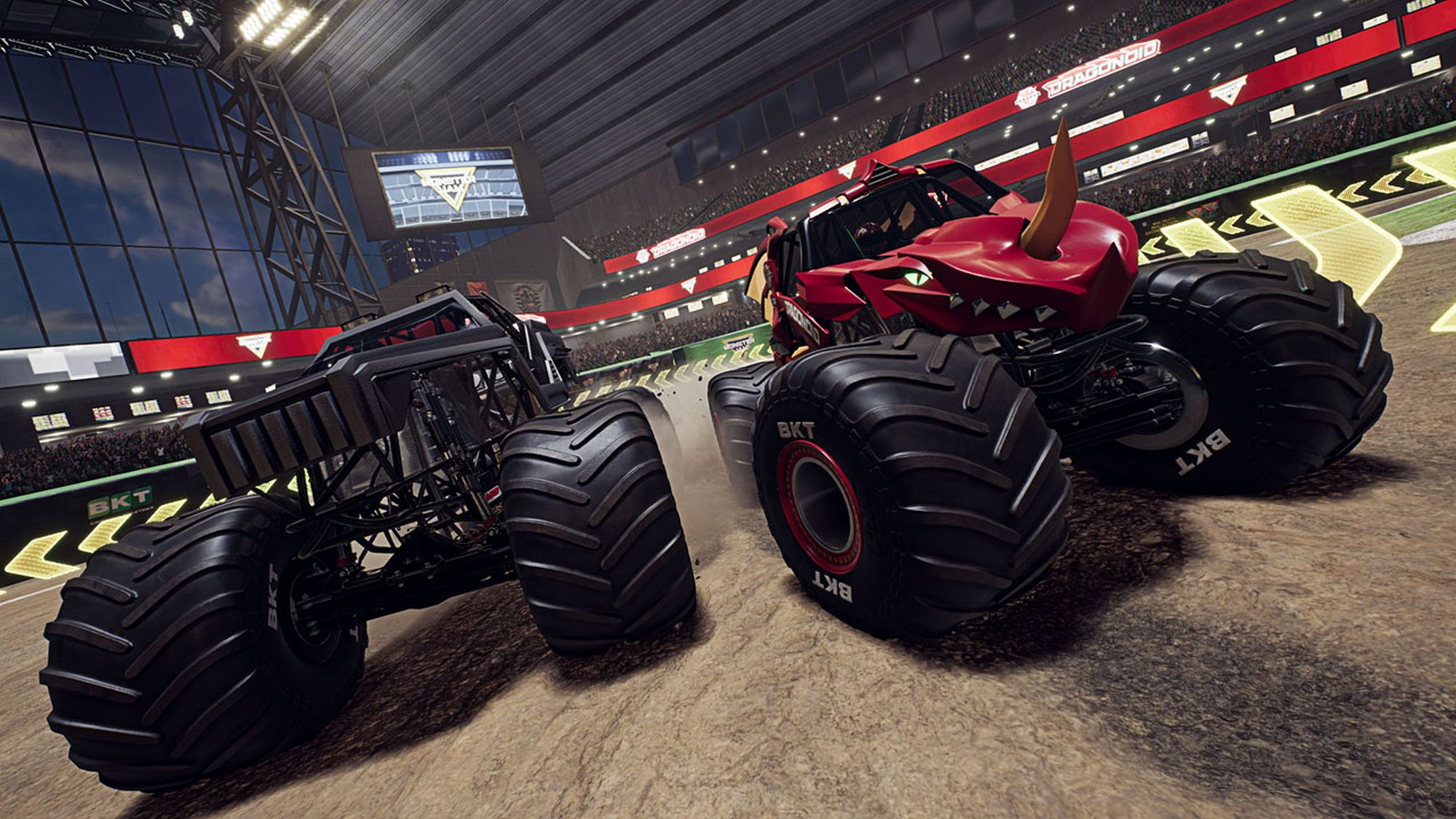 Gara di monster truck, uno rosso e uno nero, in uno stadio con pista sterrata.