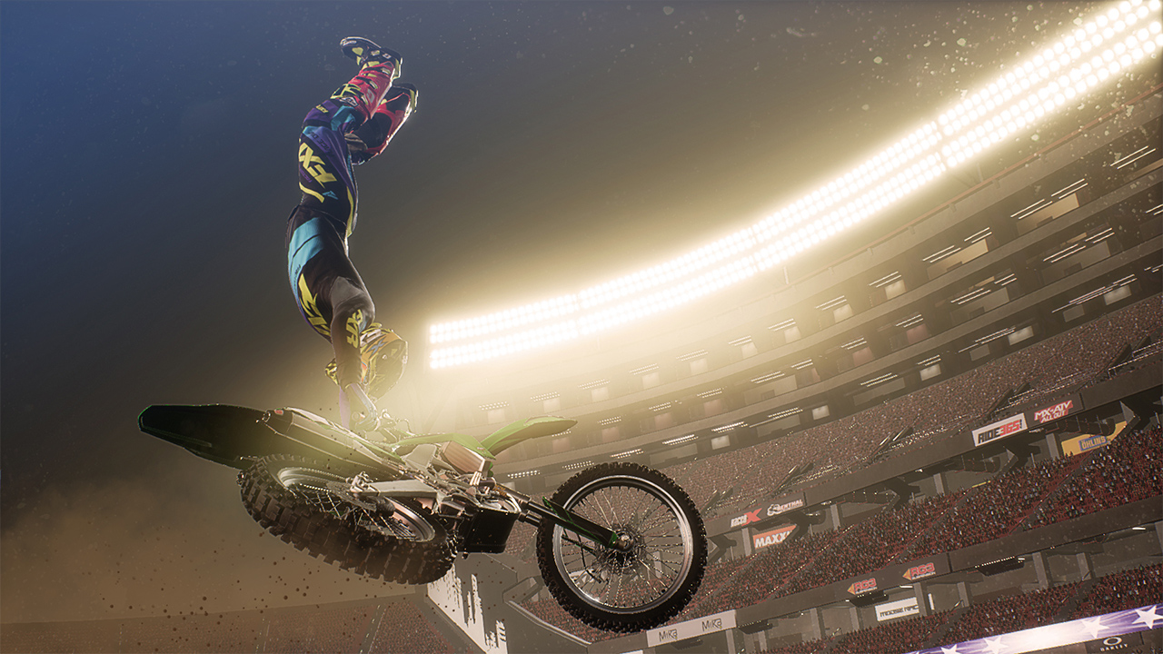 Un pilota di motocross esegue un salto mortale all'indietro su una moto verde in uno stadio. La folla guarda sotto luci intense.