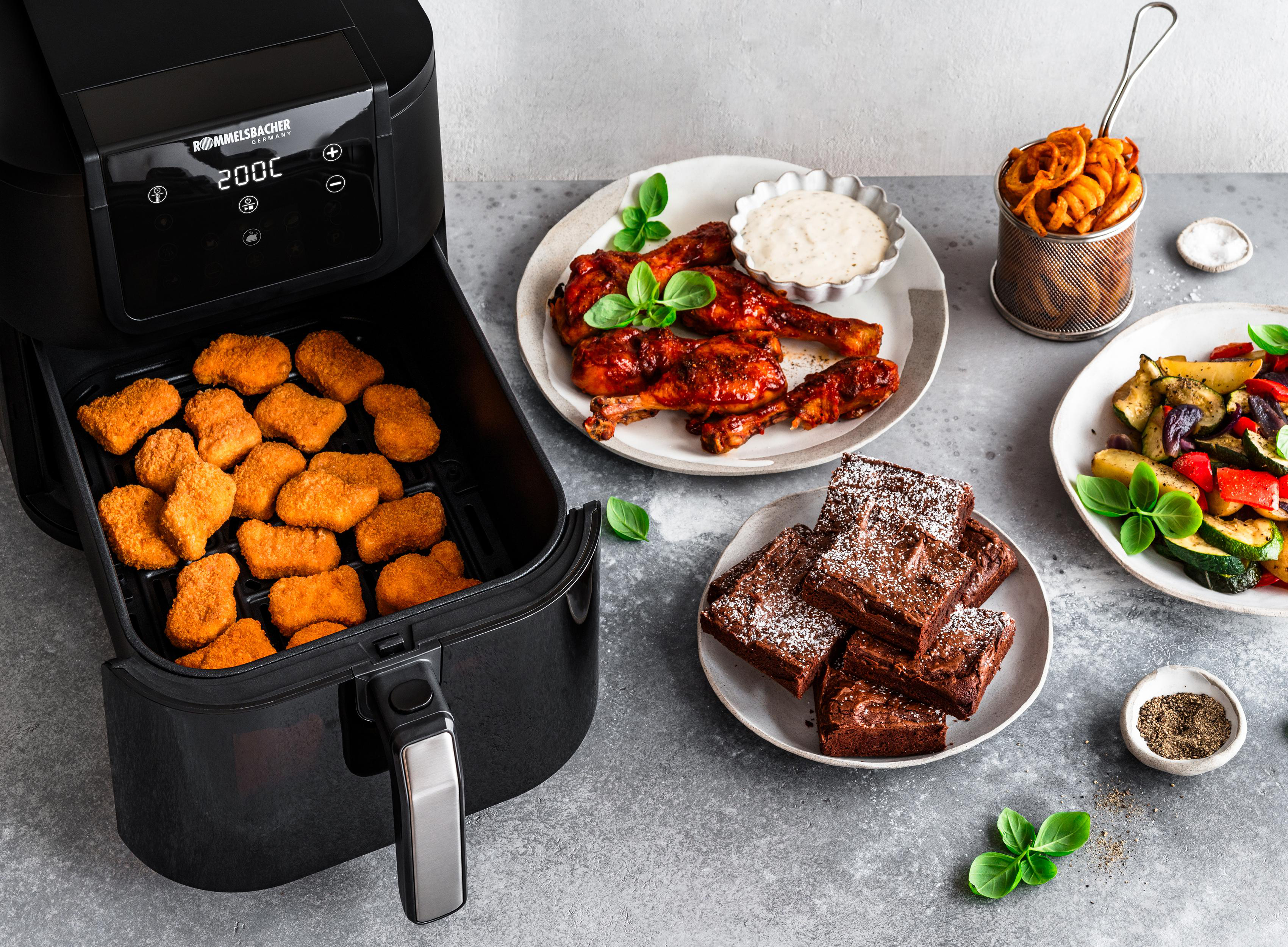 Heißluftfritteuse mit Hähnchen, Nuggets, Gemüse und Brownies auf Tellern.