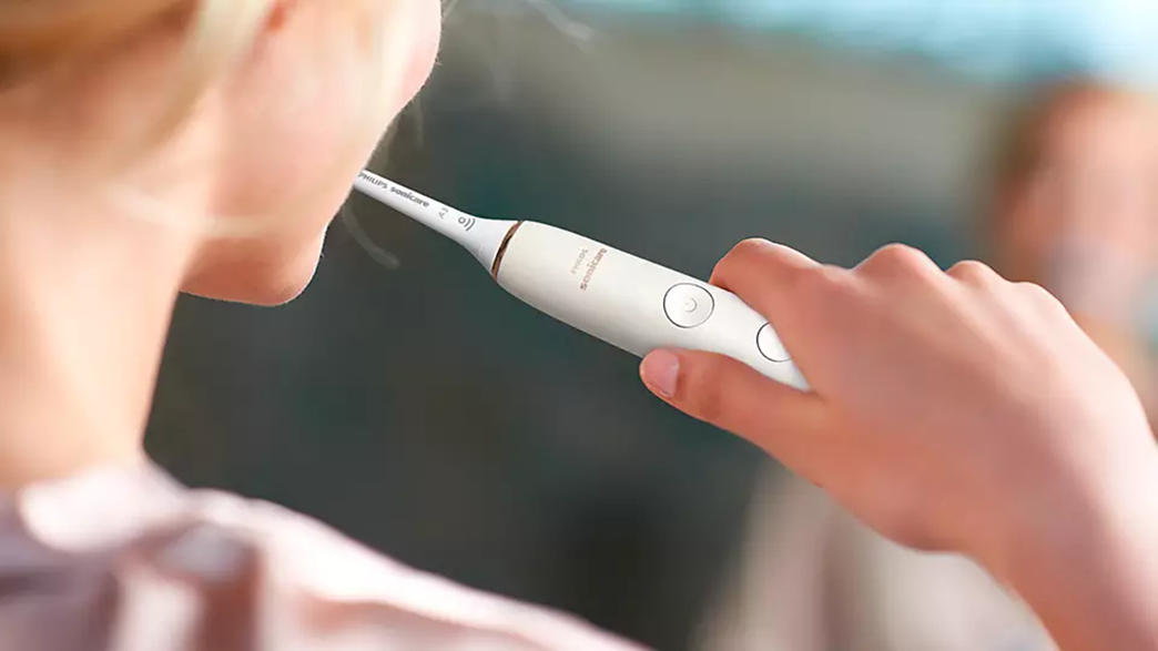 Egy személy fehér elektromos fogkefét használ. A kefe a fogai közelében van.