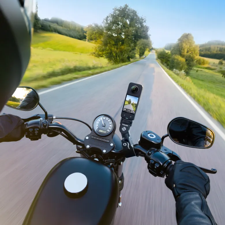 Motorradfahrer-Perspektive mit 360-Grad-Kamera am Lenker, malerische Straße im Hintergrund.
