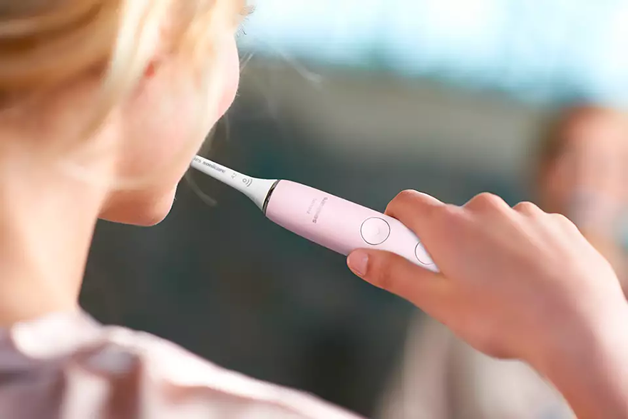 Egy nő rózsaszín elektromos fogkefével mos fogat.