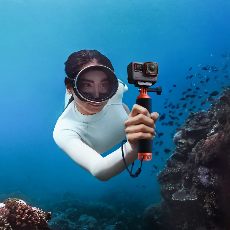 Frau unter Wasser mit Tauchmaske hält Kamera in orangefarbenem Gehäuse.