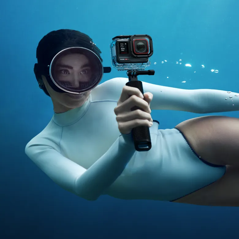 Persona sott'acqua con attrezzatura subacquea, tiene una fotocamera.
