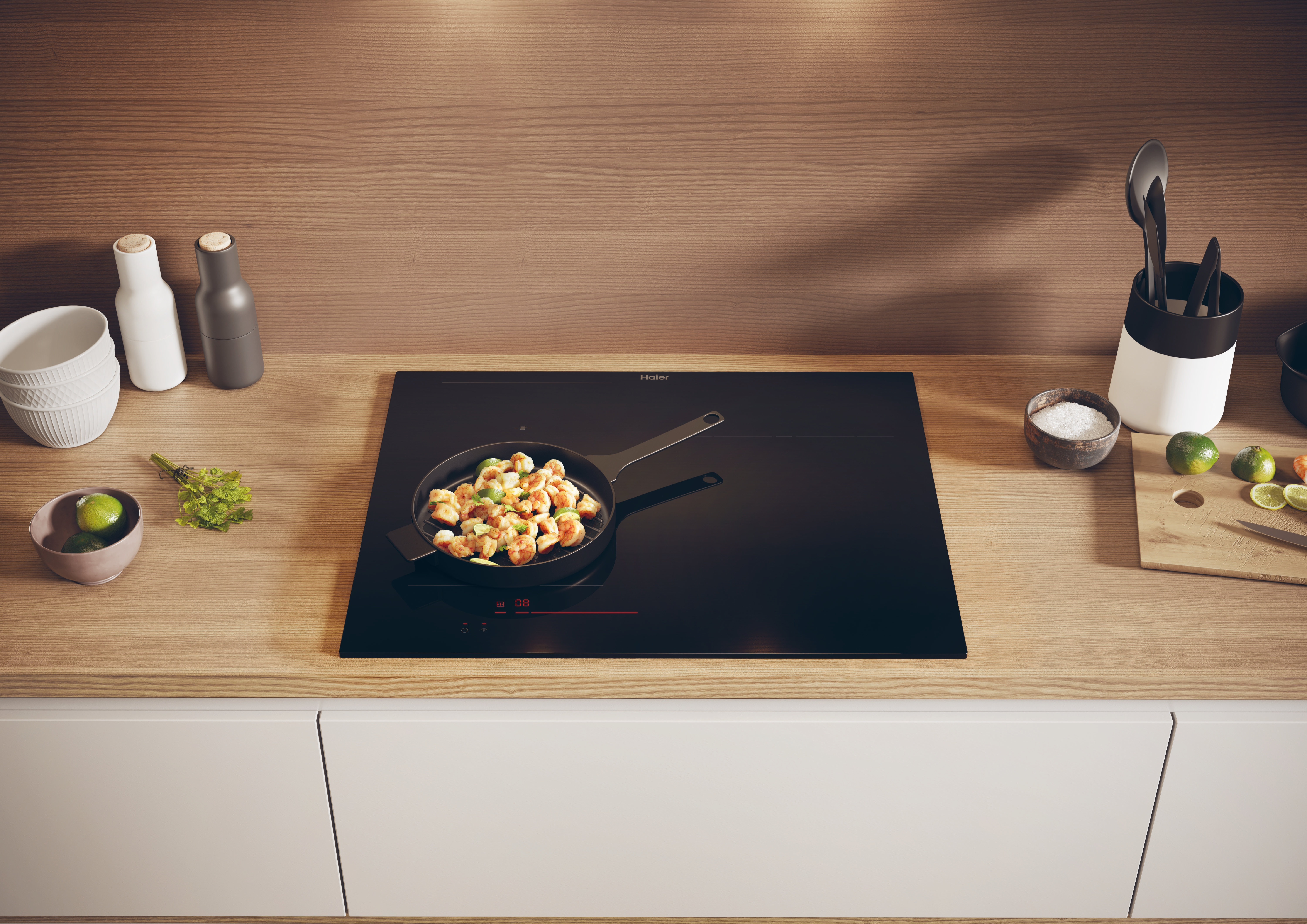 Escena de cocina: Placa con sartén de comida, ingredientes y utensilios sobre encimera de madera. Armarios blancos debajo.