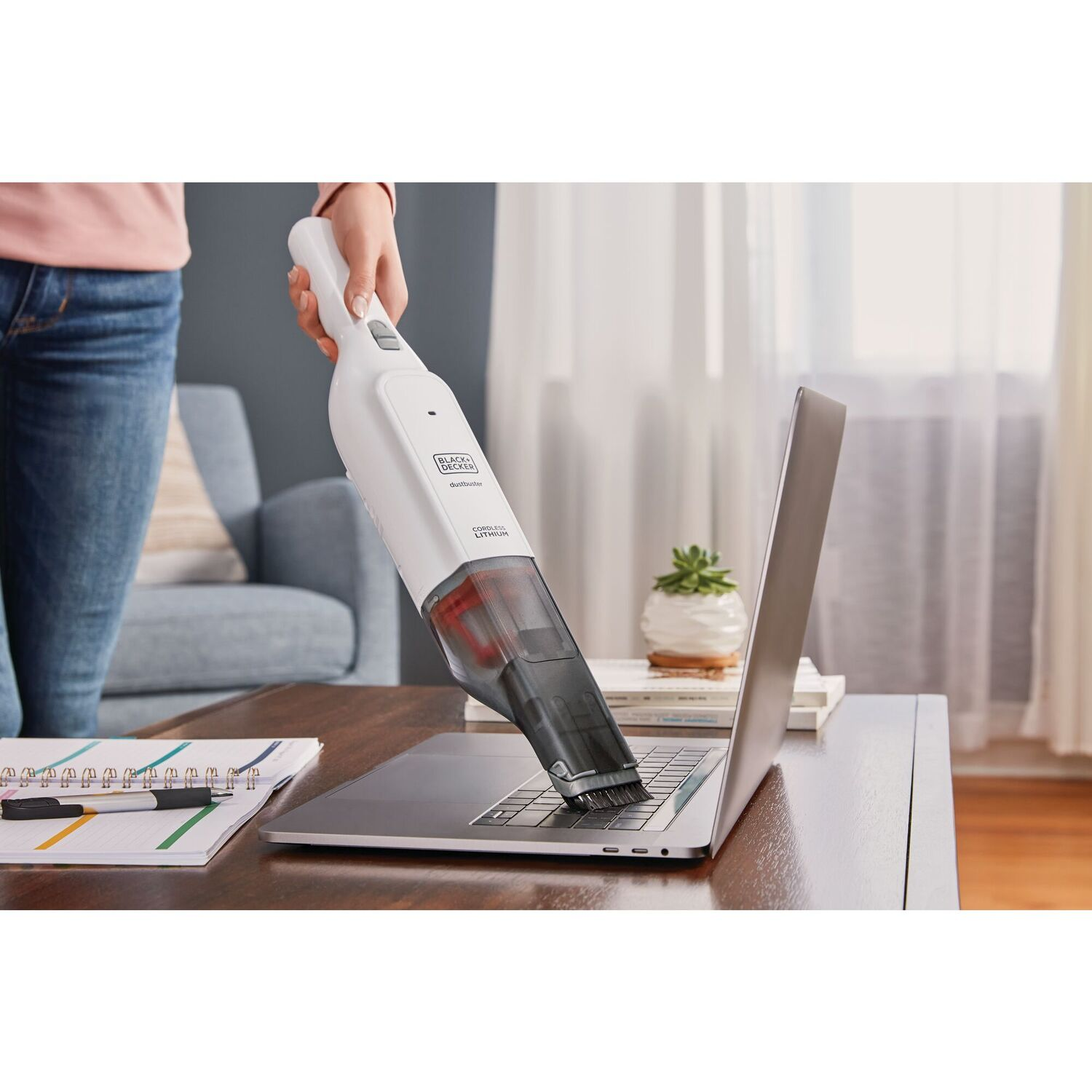 A person vacuuming a laptop keyboard with a white Black+Decker vacuum.