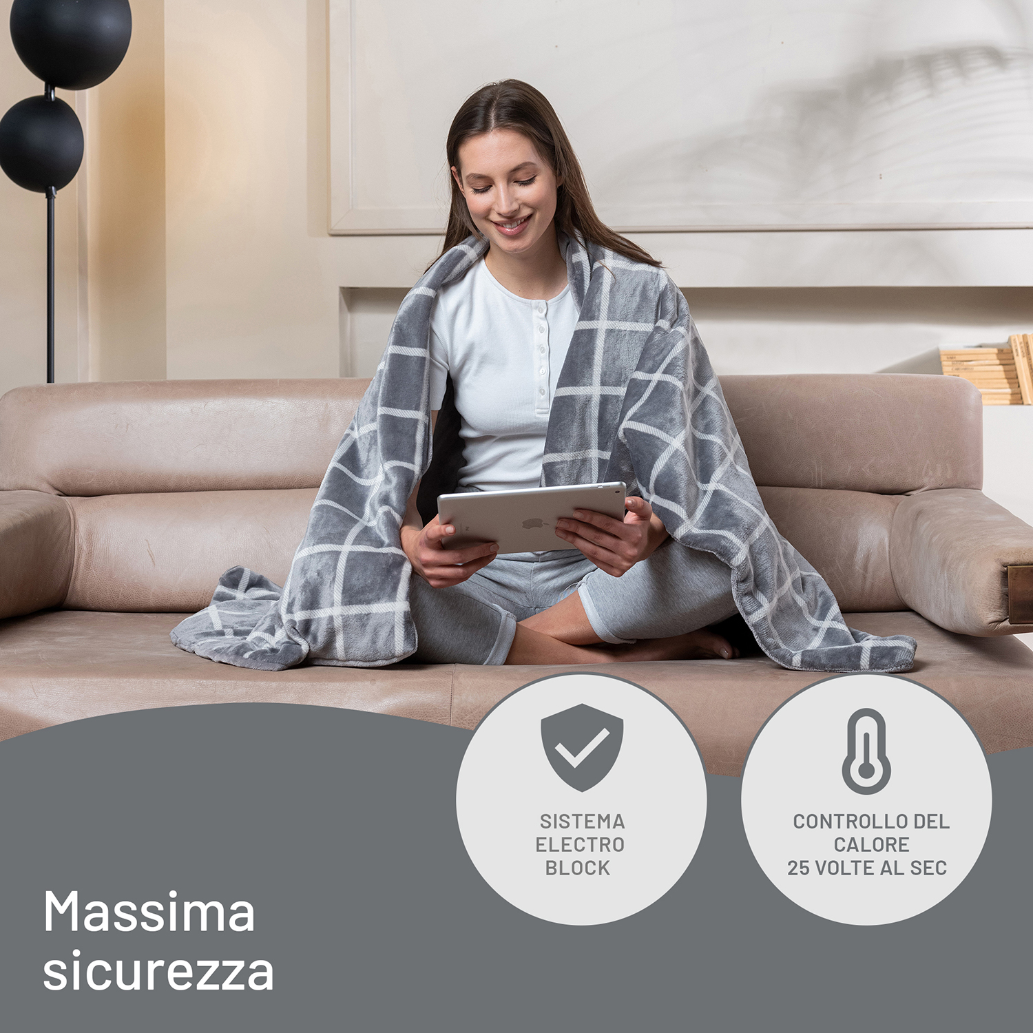 Donna sul divano con tablet, coperta da coperta grigia. Sfondo: lampade, arte murale e testo.