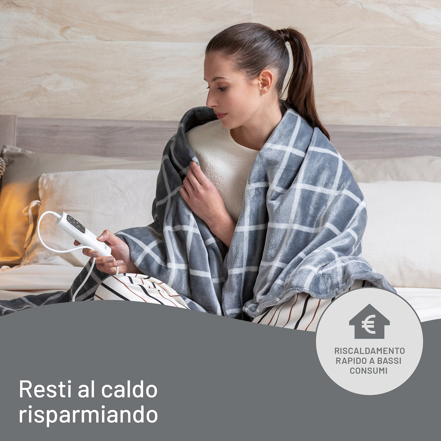 Donna seduta, avvolta in una coperta elettrica a quadri, tiene pannello comandi su letto.