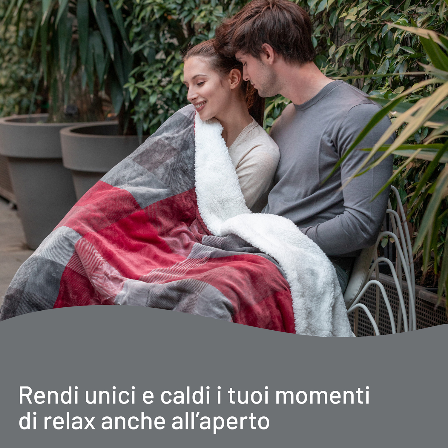 Coppia che si abbraccia sotto una coperta a quadri rossa e grigia su una sedia bianca.