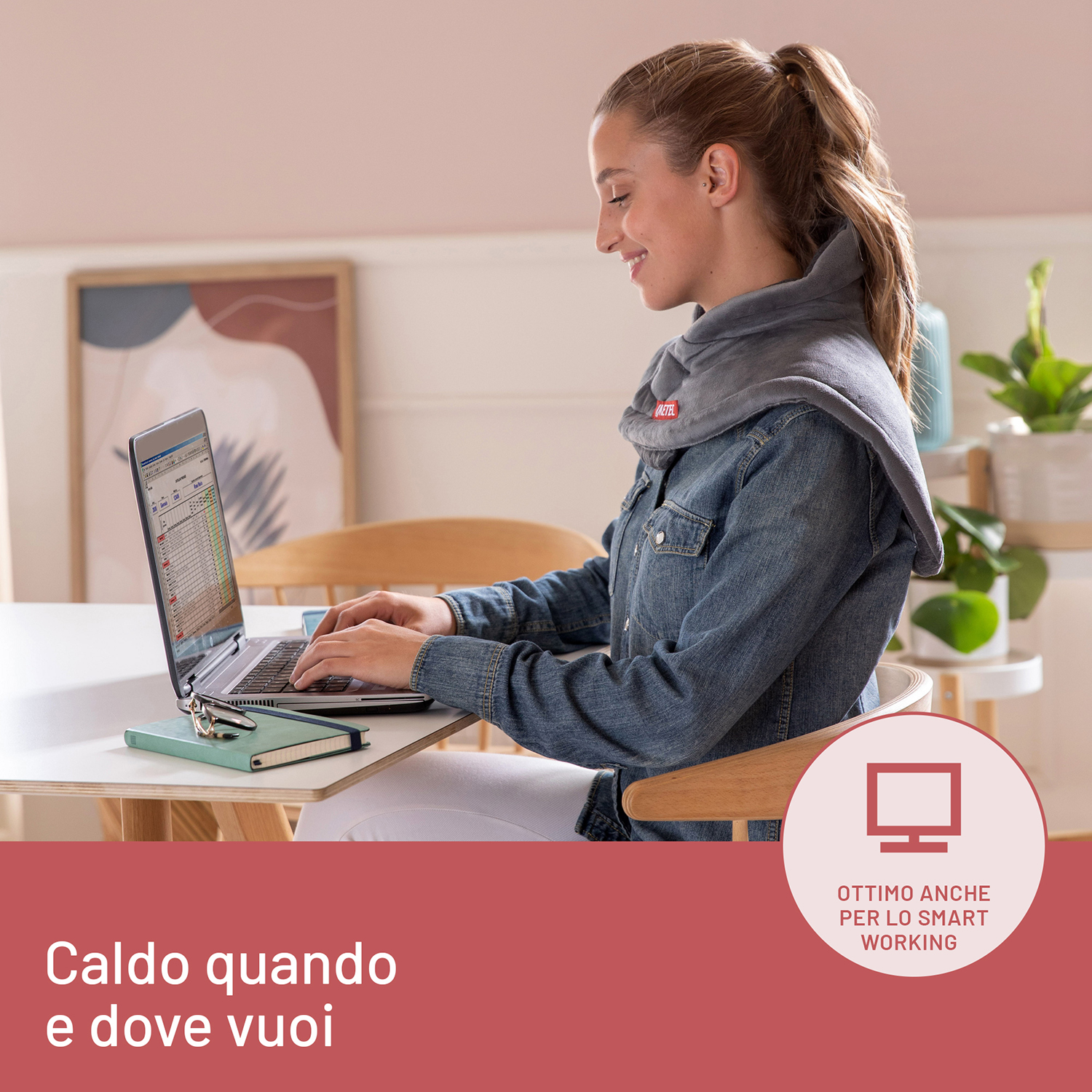 Una donna lavora su un laptop con un cuscinetto termico per il collo, sorridendo in una stanza ben illuminata.