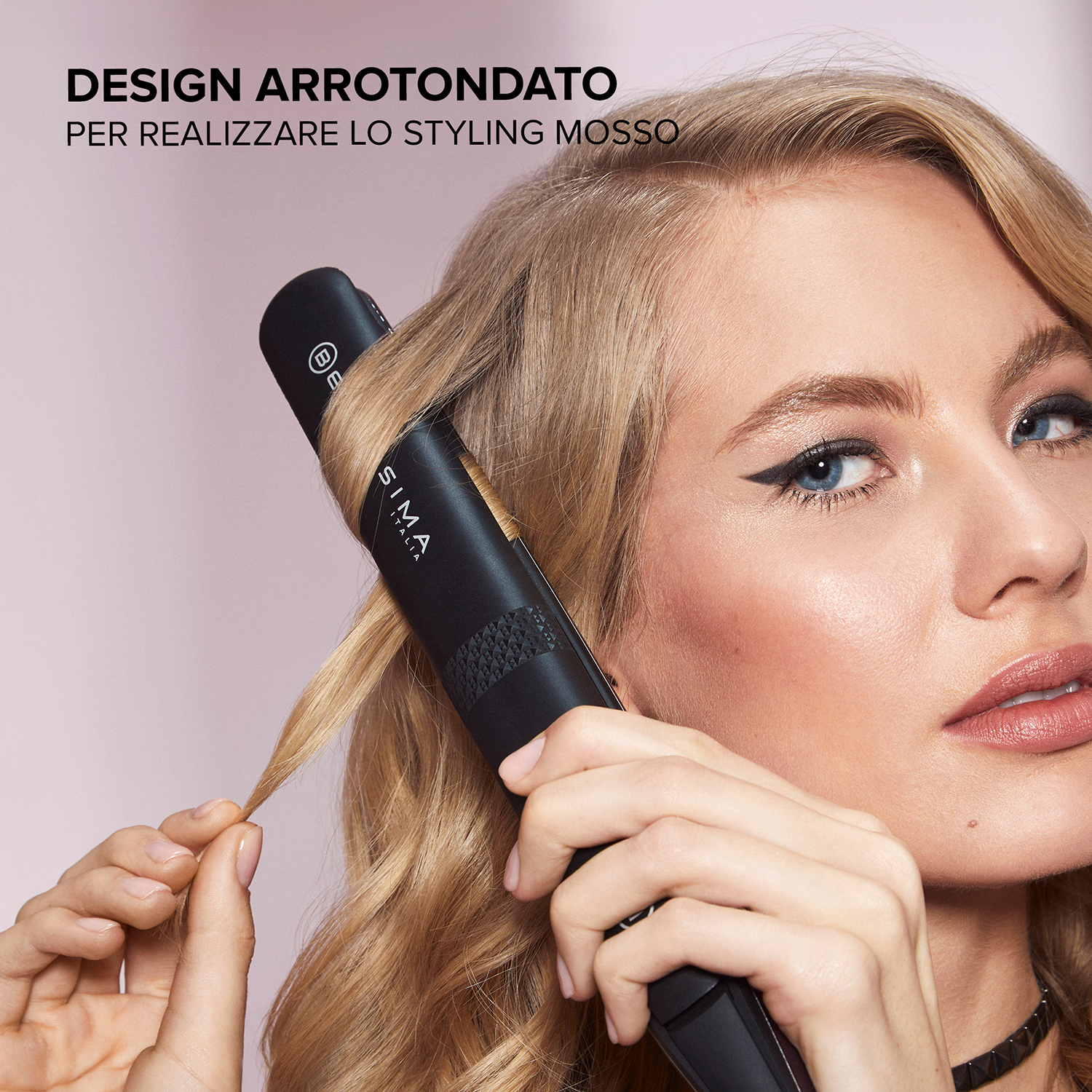 Donna che si acconcia i capelli con un arricciacapelli. Capelli biondi, arricciacapelli nero e testo presenti.