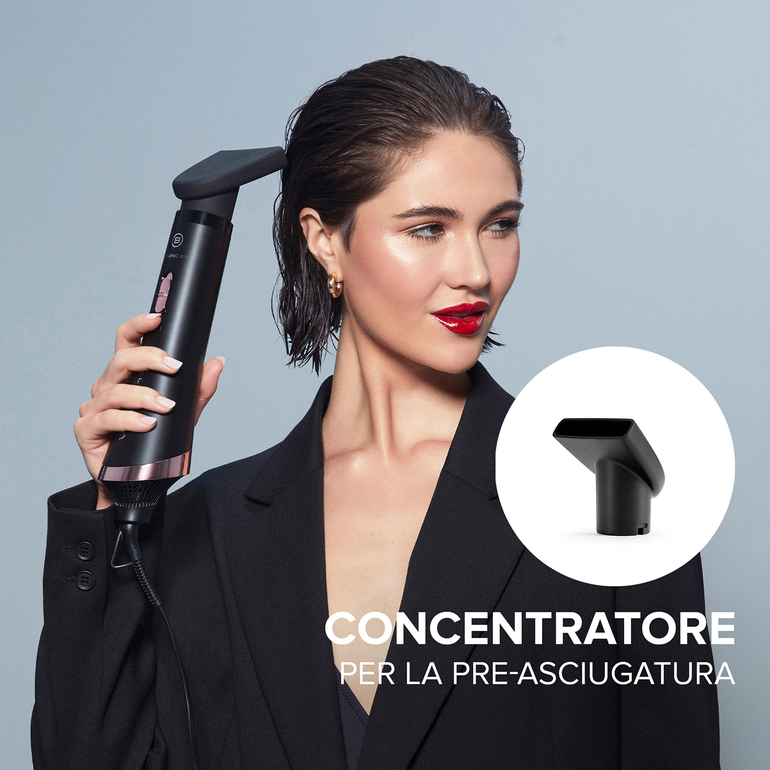 Donna che si asciuga i capelli con un asciugacapelli nero e oro rosa, con un accessorio focalizzato in basso a destra.