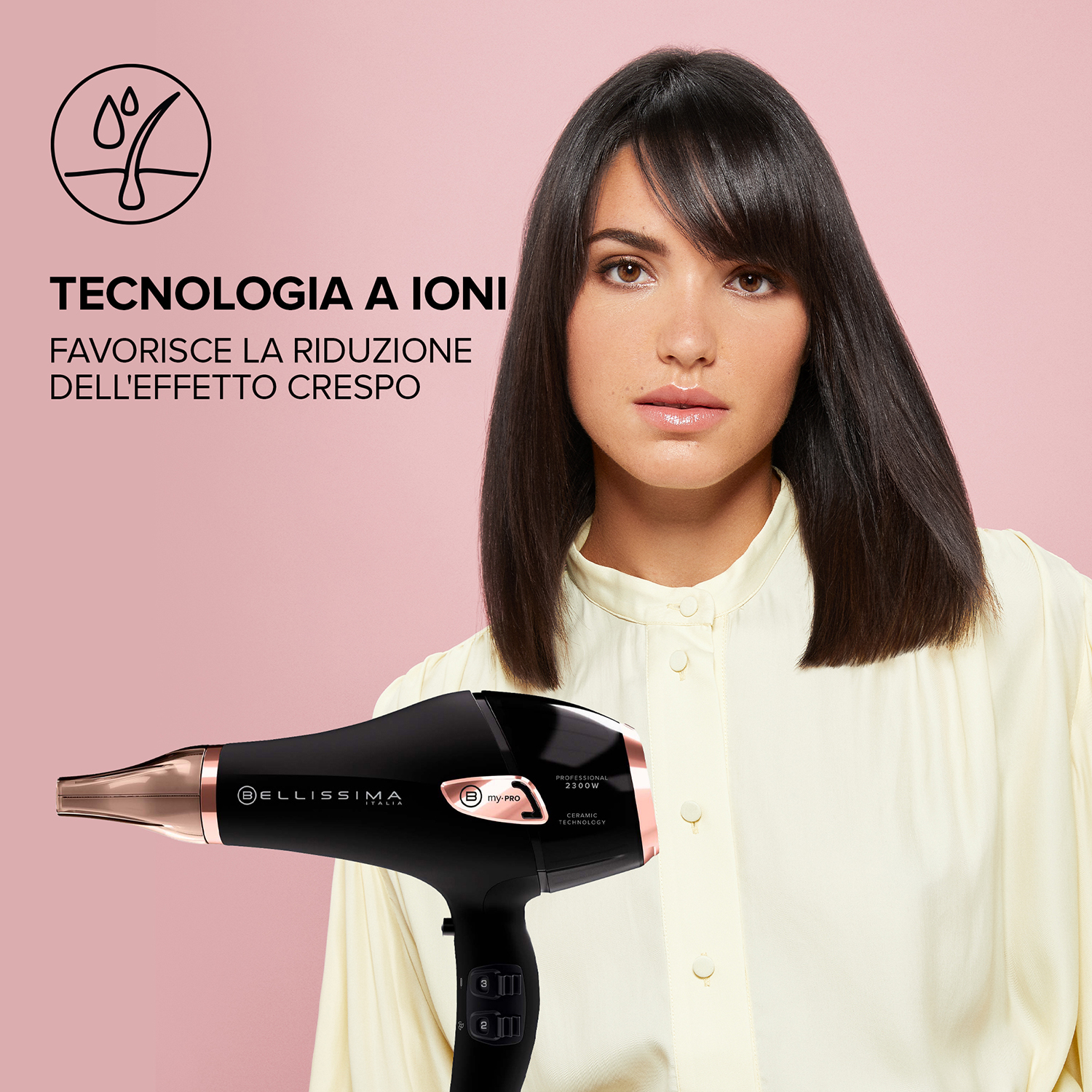 Una donna con i capelli scuri tiene un asciugacapelli nero e oro rosa davanti a uno sfondo rosa.