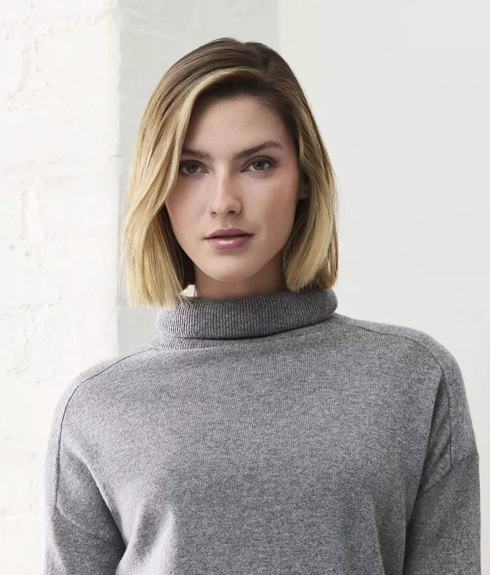 Kobieta w szarym swetrze z golfem, patrząca w przód, z blond włosami.