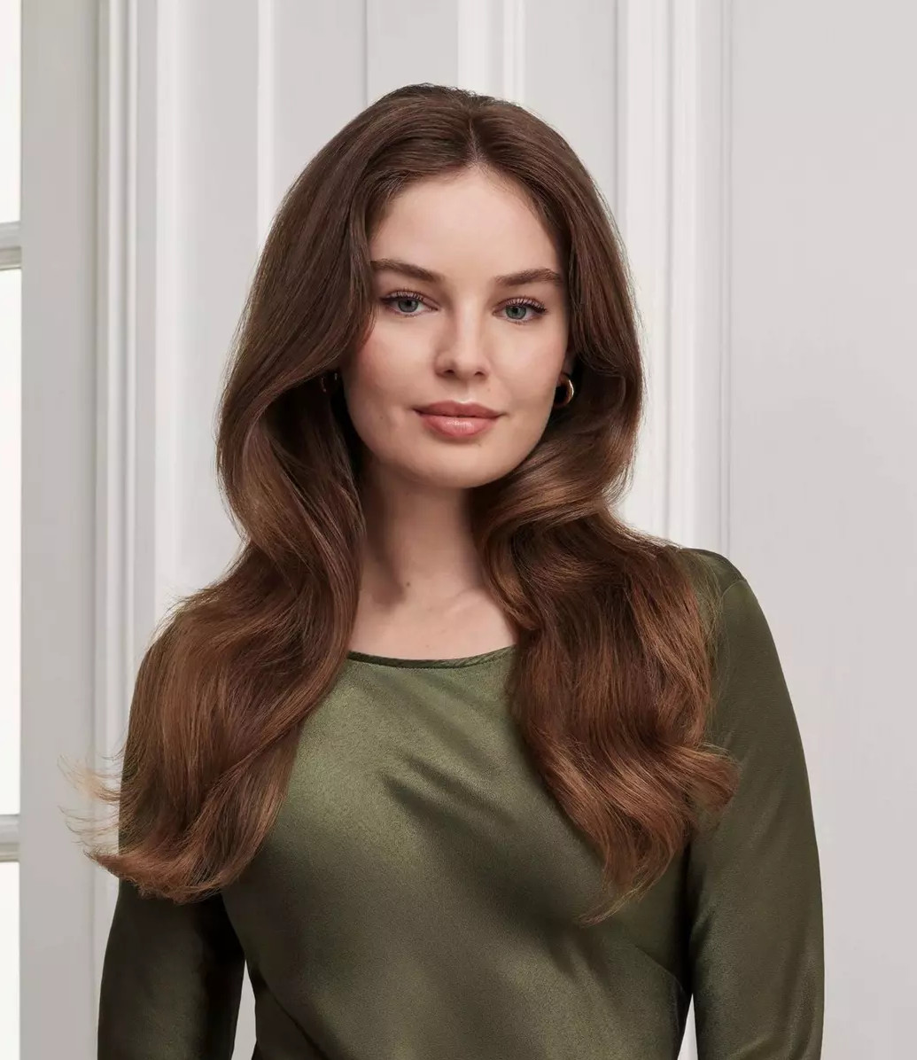 Kobieta z długimi, falowanymi brązowymi włosami i zieloną bluzką, patrząca w kamerę.