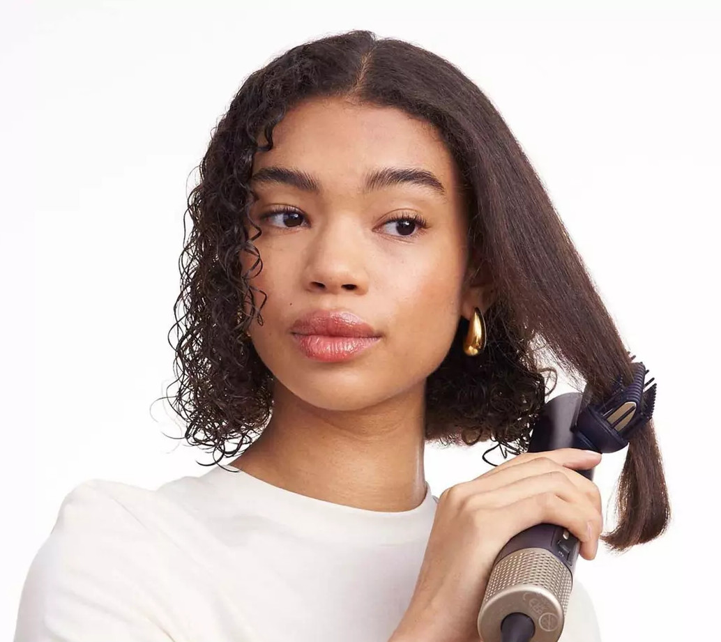 Kobieta stylizuje włosy szczotką do kręcenia. Ma kręcone włosy i uśmiecha się.