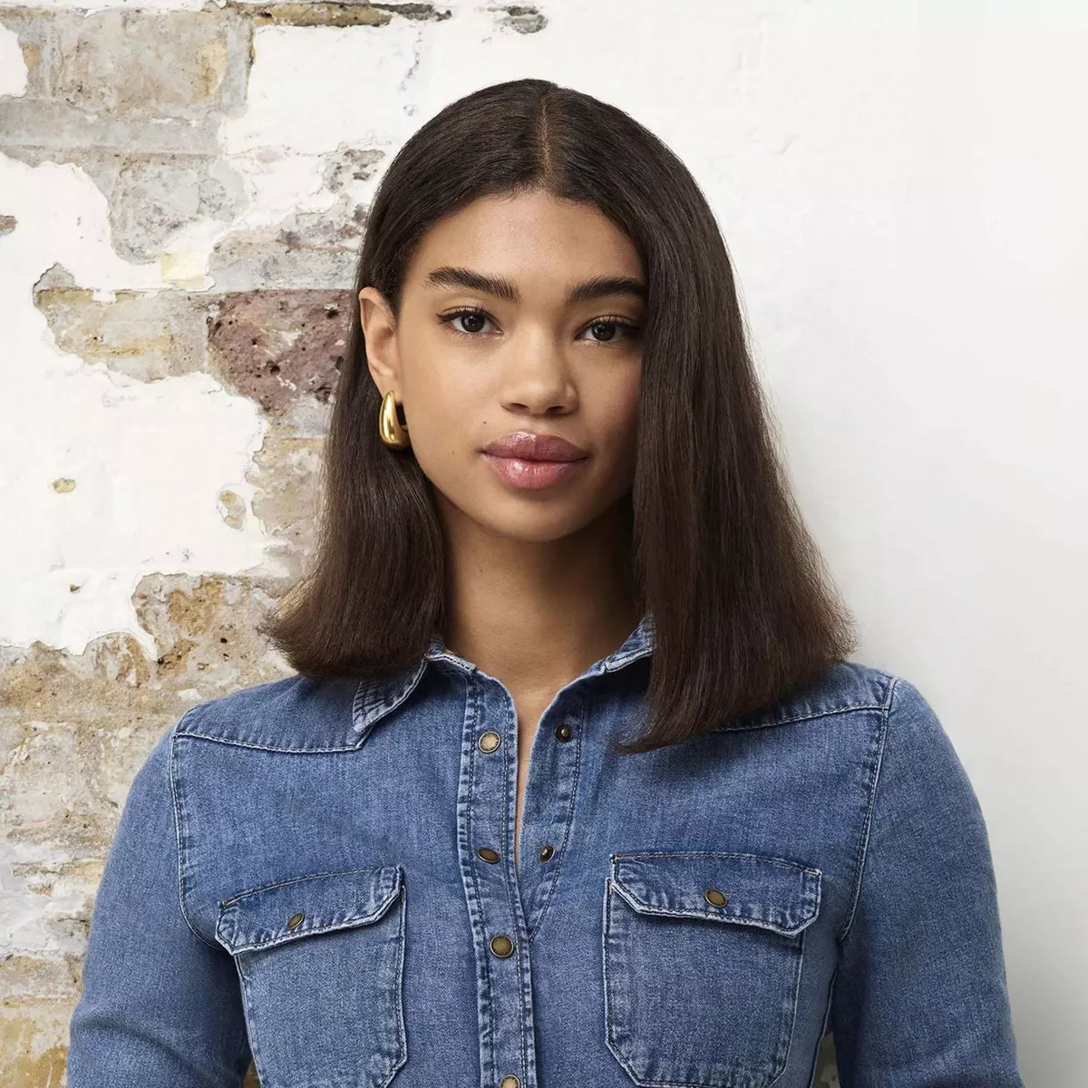Kobieta z krótkimi, ciemnobrązowymi włosami i złotymi kolczykami kołami, w koszuli dżinsowej, patrząca w kamerę.