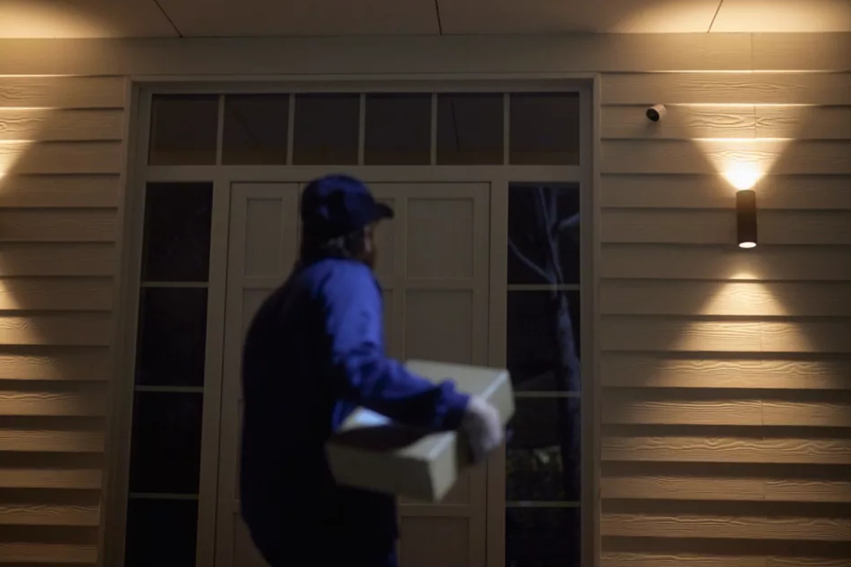 Dostawca pod drzwiami domu trzymający paczkę. Zewnętrze z włączonymi światłami.