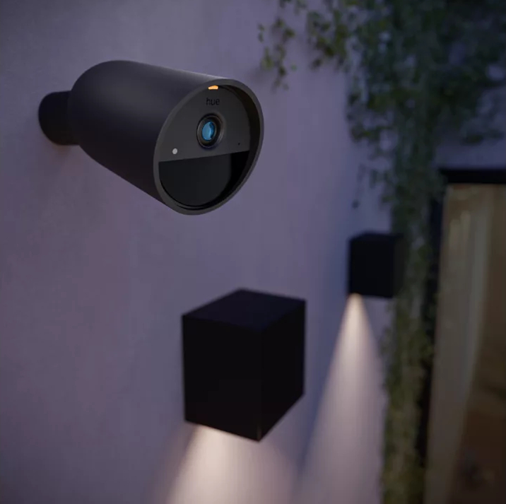 Czarna kamera bezpieczeństwa i światła na ścianie. Ściana jest jasnofioletowa.