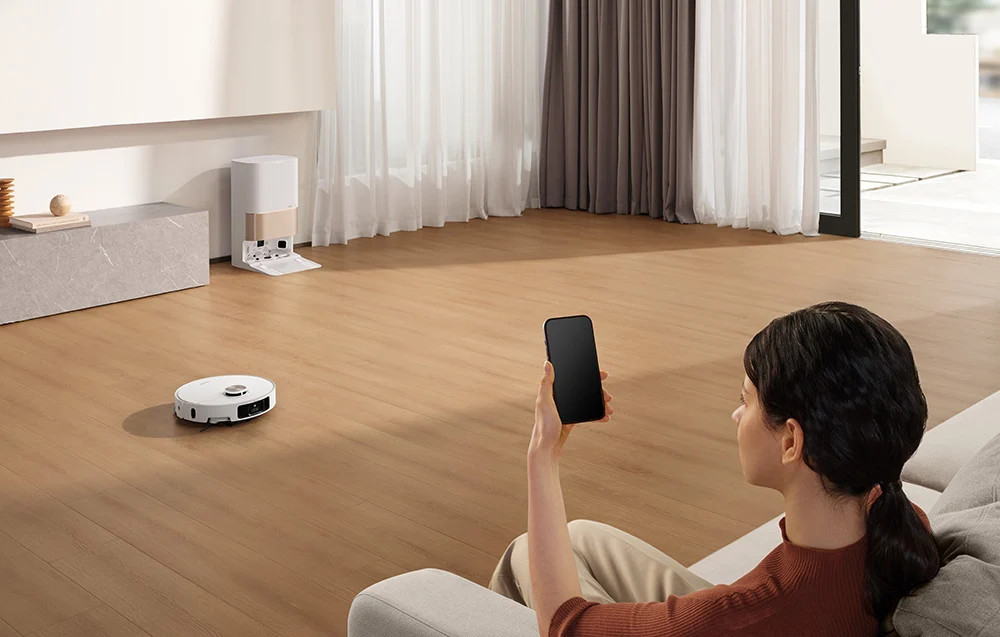 Kobieta obsługująca robota sprzątającego za pomocą smartfona.