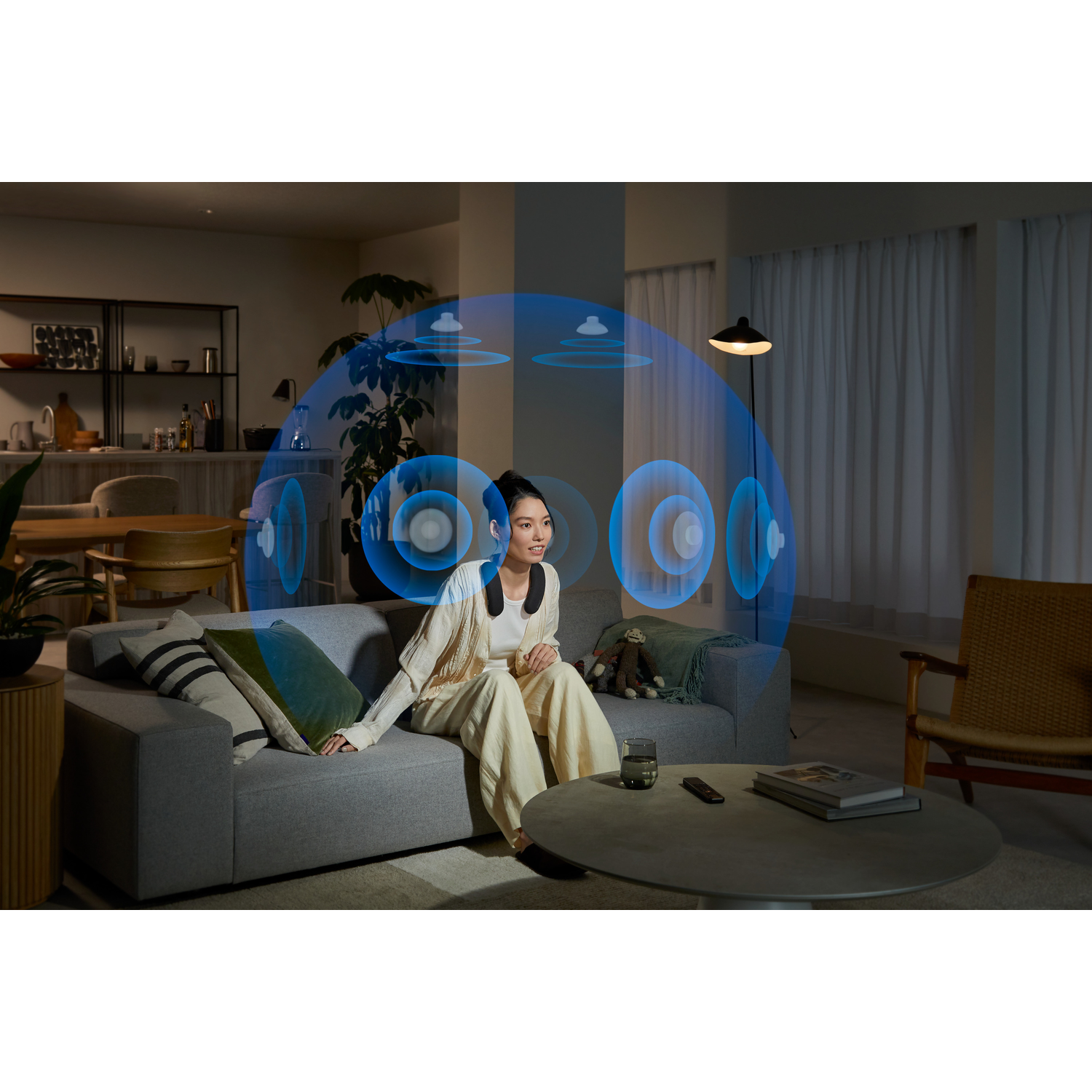 A woman wearing a neck speaker sitting on a sofa.