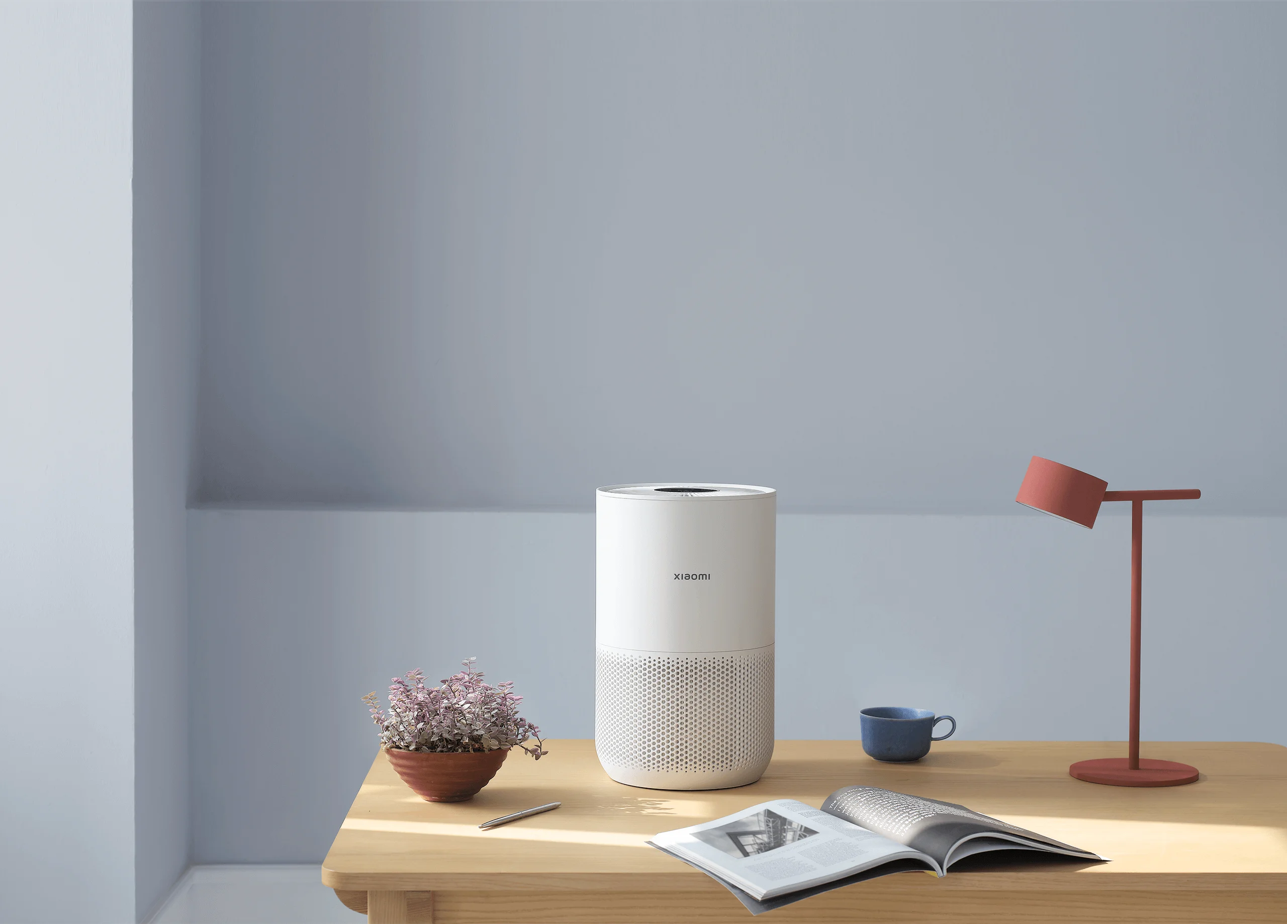 Purificateur d'air blanc, table et lampe dans une pièce avec un mur bleu. Aussi un magazine.