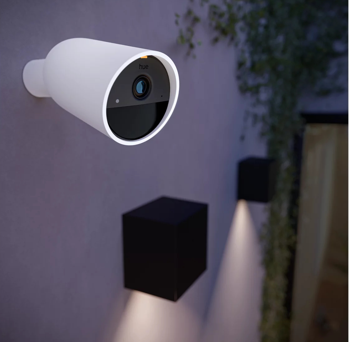 Biała kamera monitoringu na ścianie. Dwie czarne lampy znajdują się poniżej na ścianie.