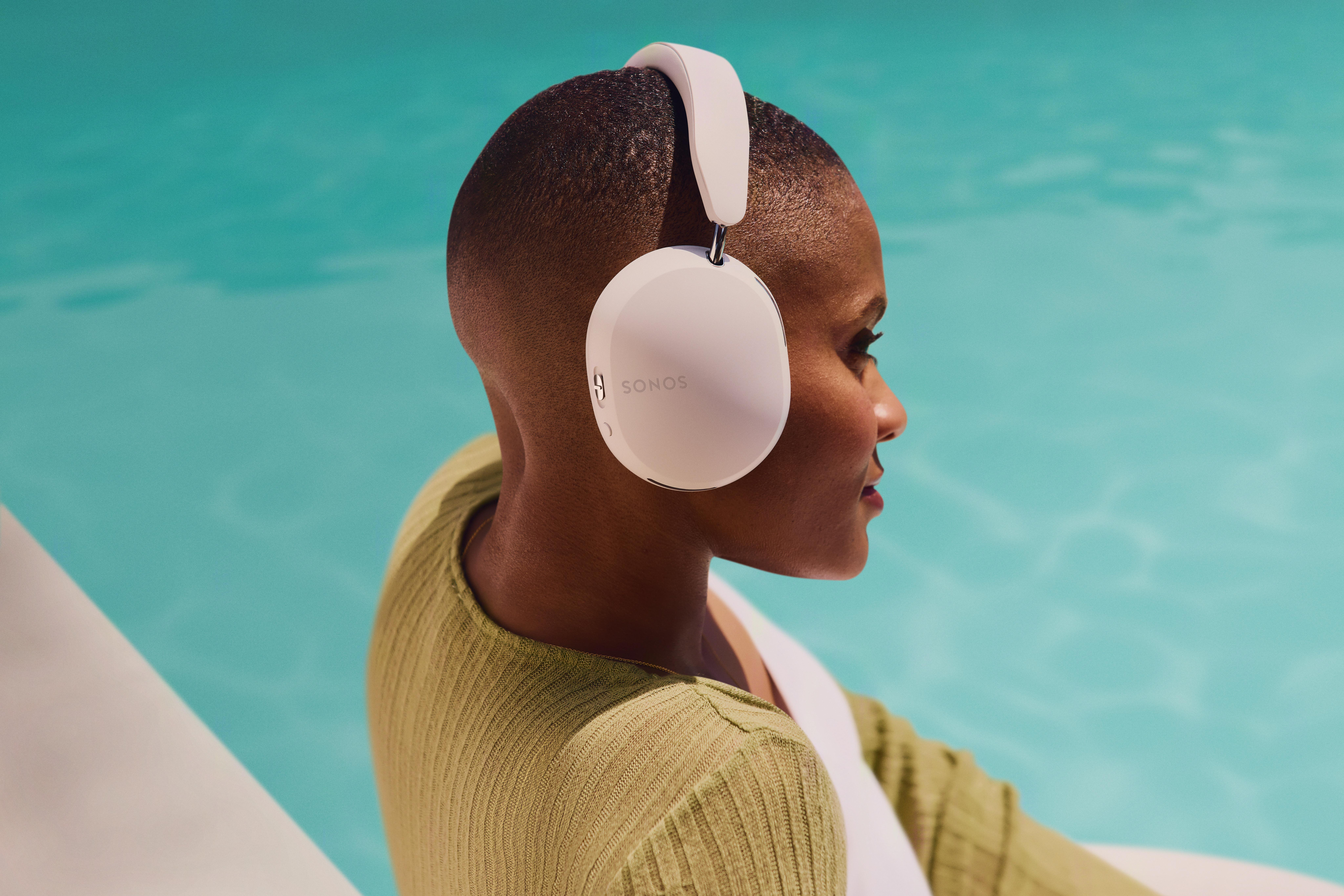 Eine Frau mit kurzen dunklen Haaren, die weiße Kopfhörer trägt, sitzt an einem Pool.