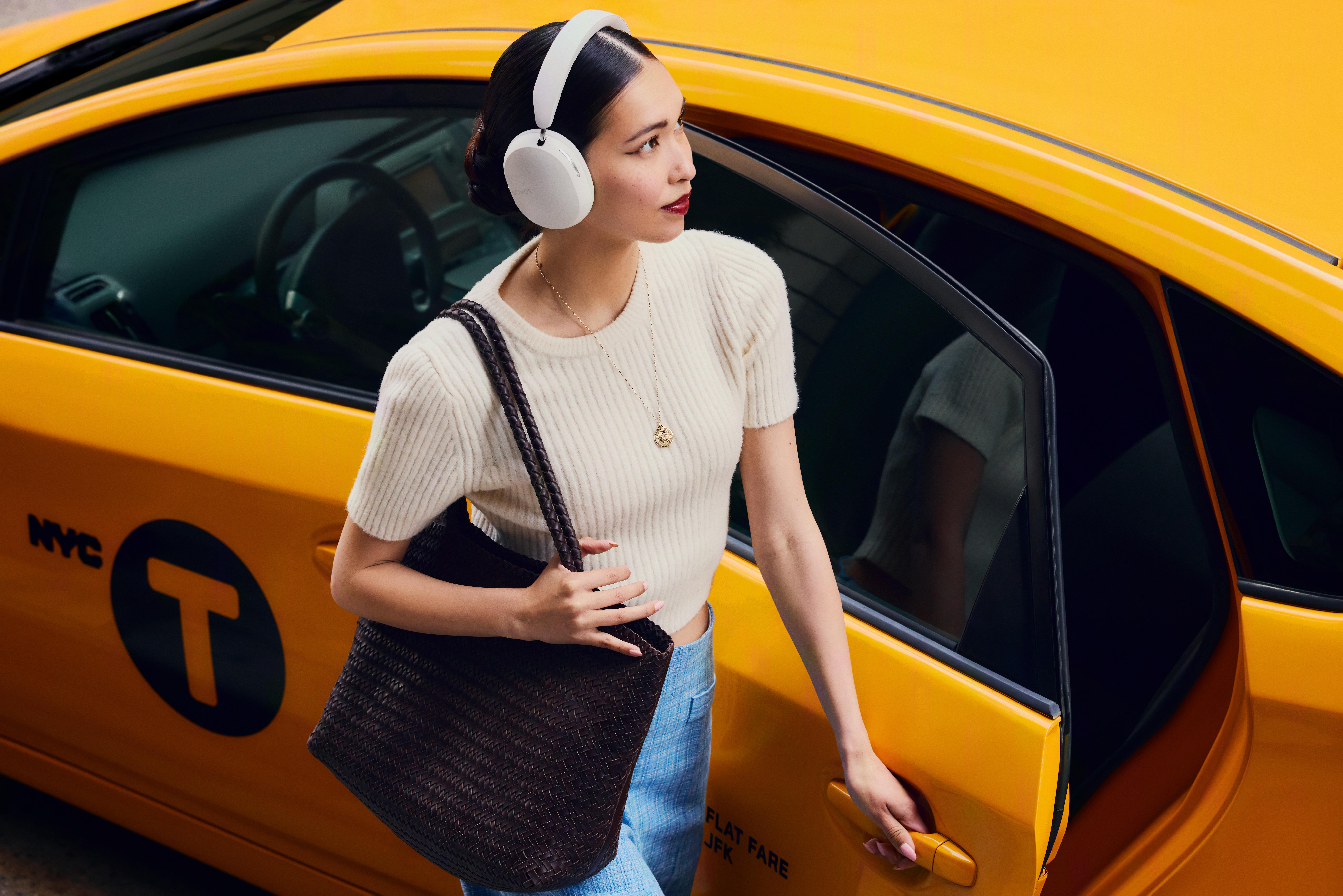 Frau steigt aus gelbem Taxi aus, Kopfhörer, Tasche. Geöffnete Tür. NYC, JFK auf Tür.